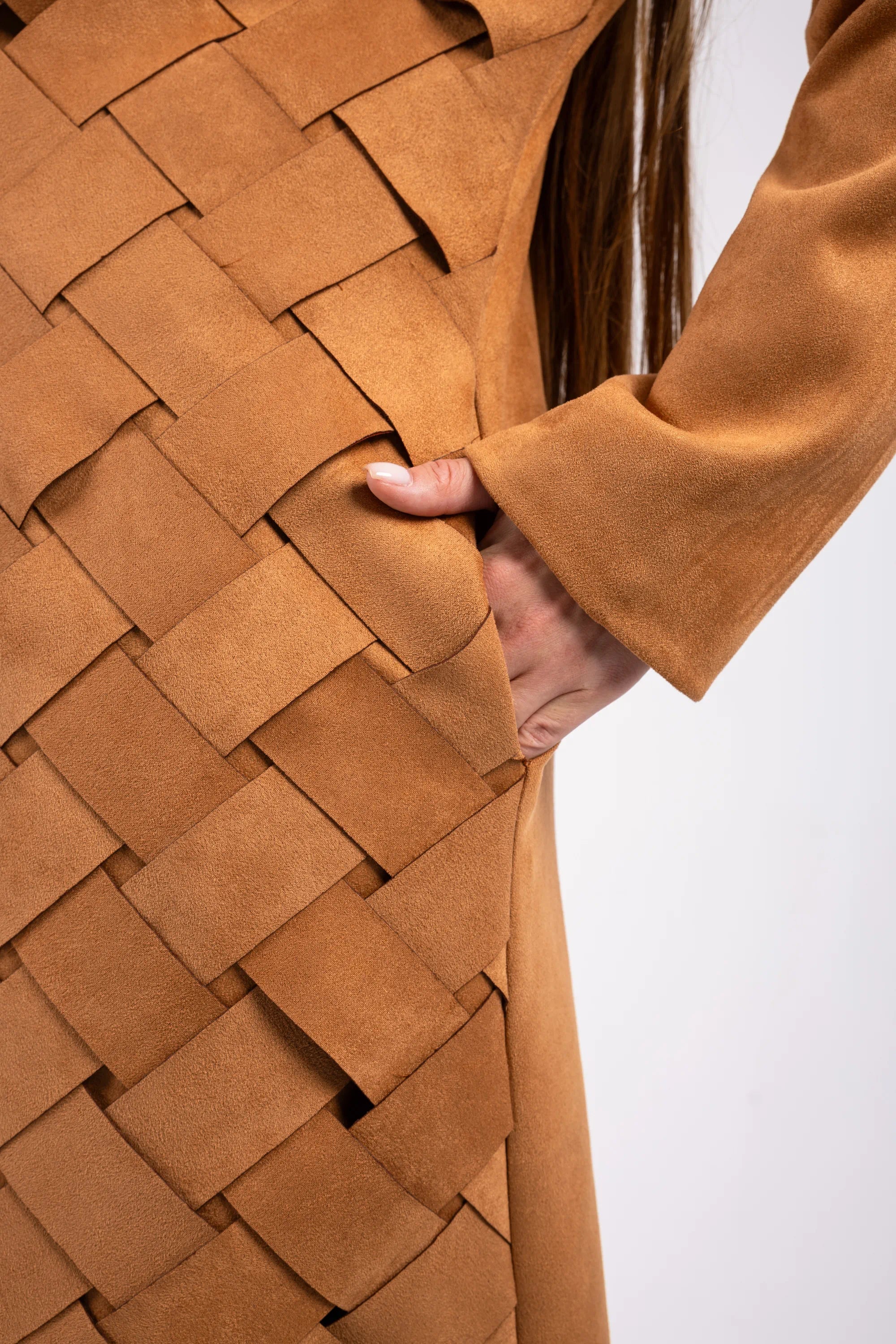 Close-up of a brown woven fabric garment with a hand touching it against a white background