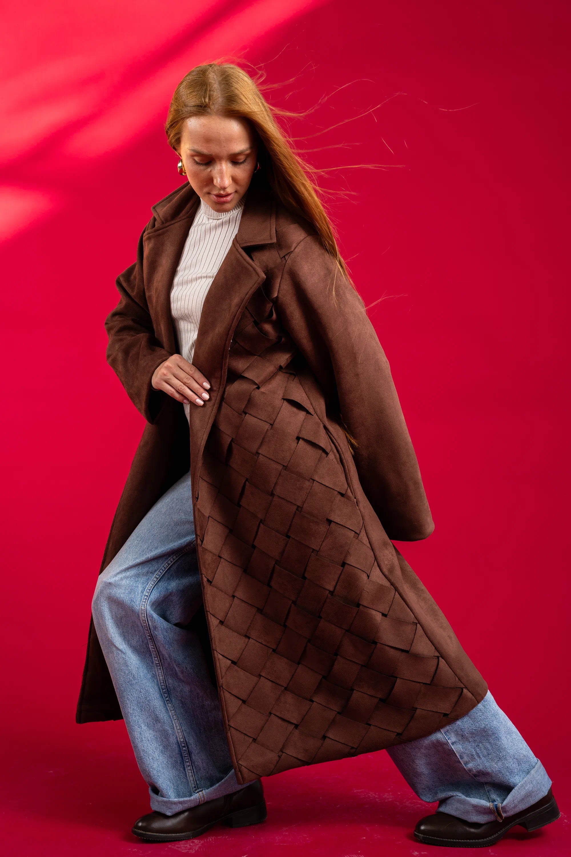 Woman wearing a brown coat and blue jeans against a red background