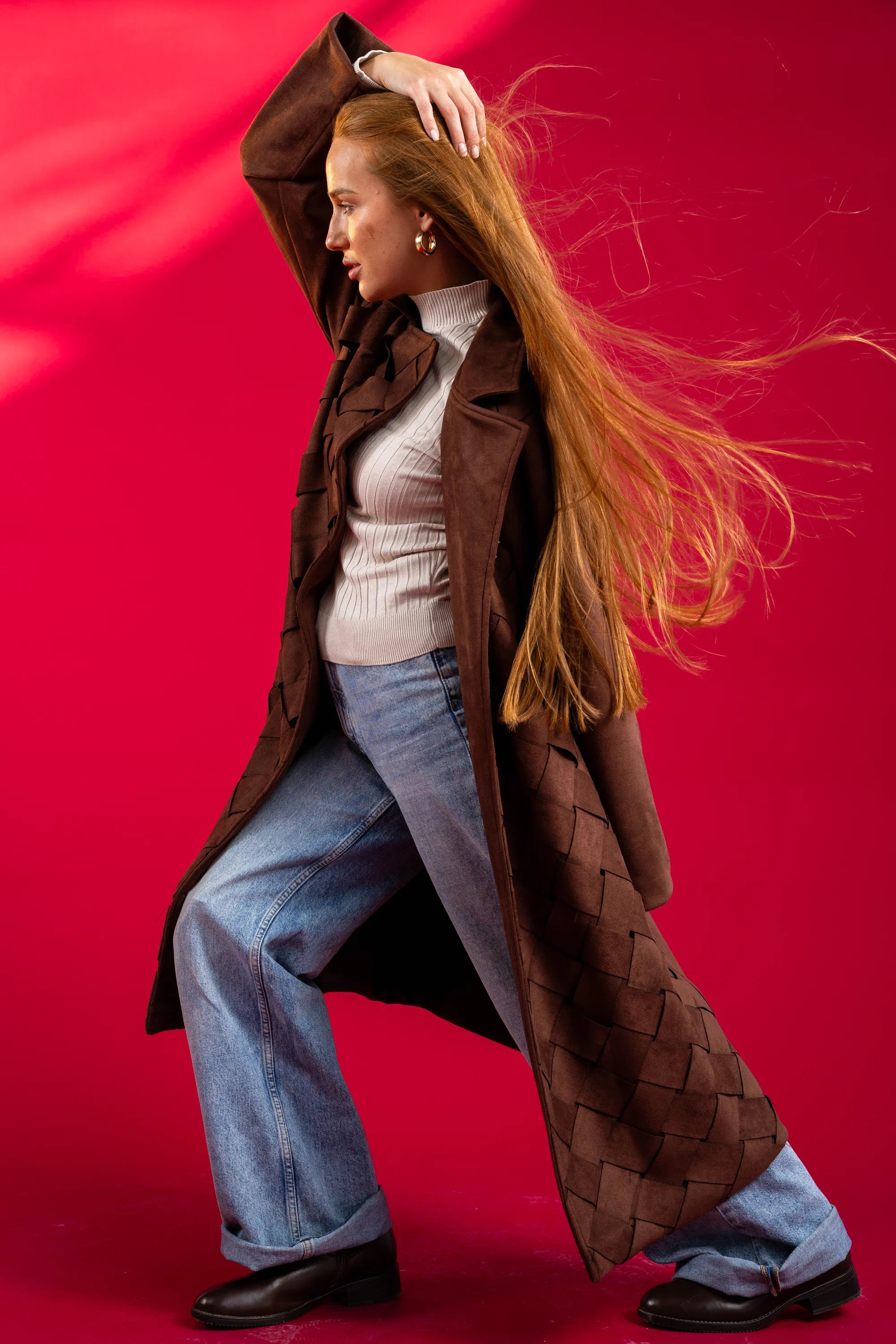 Person wearing a long brown coat against a red background