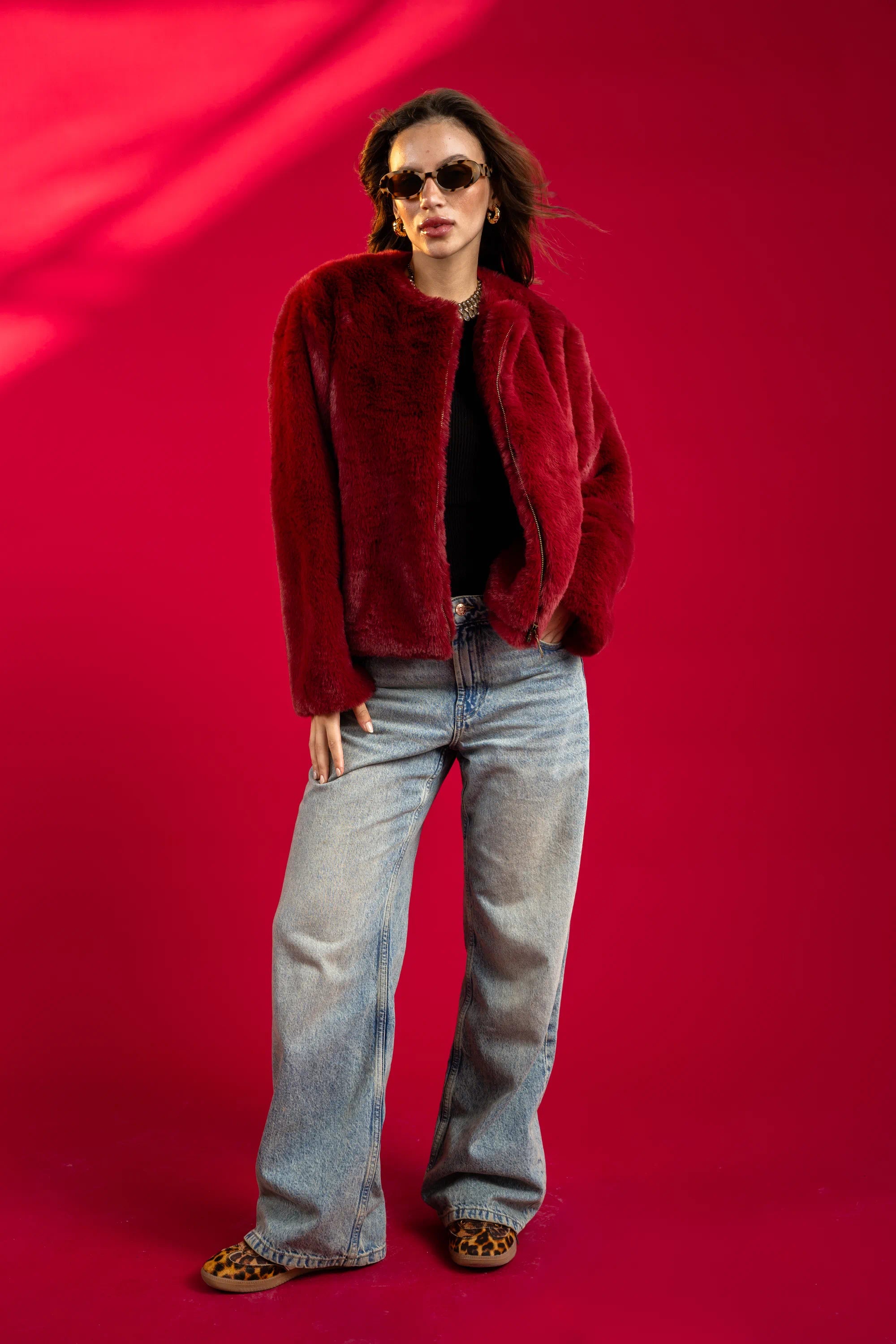Person wearing a red jacket and blue jeans against a red background