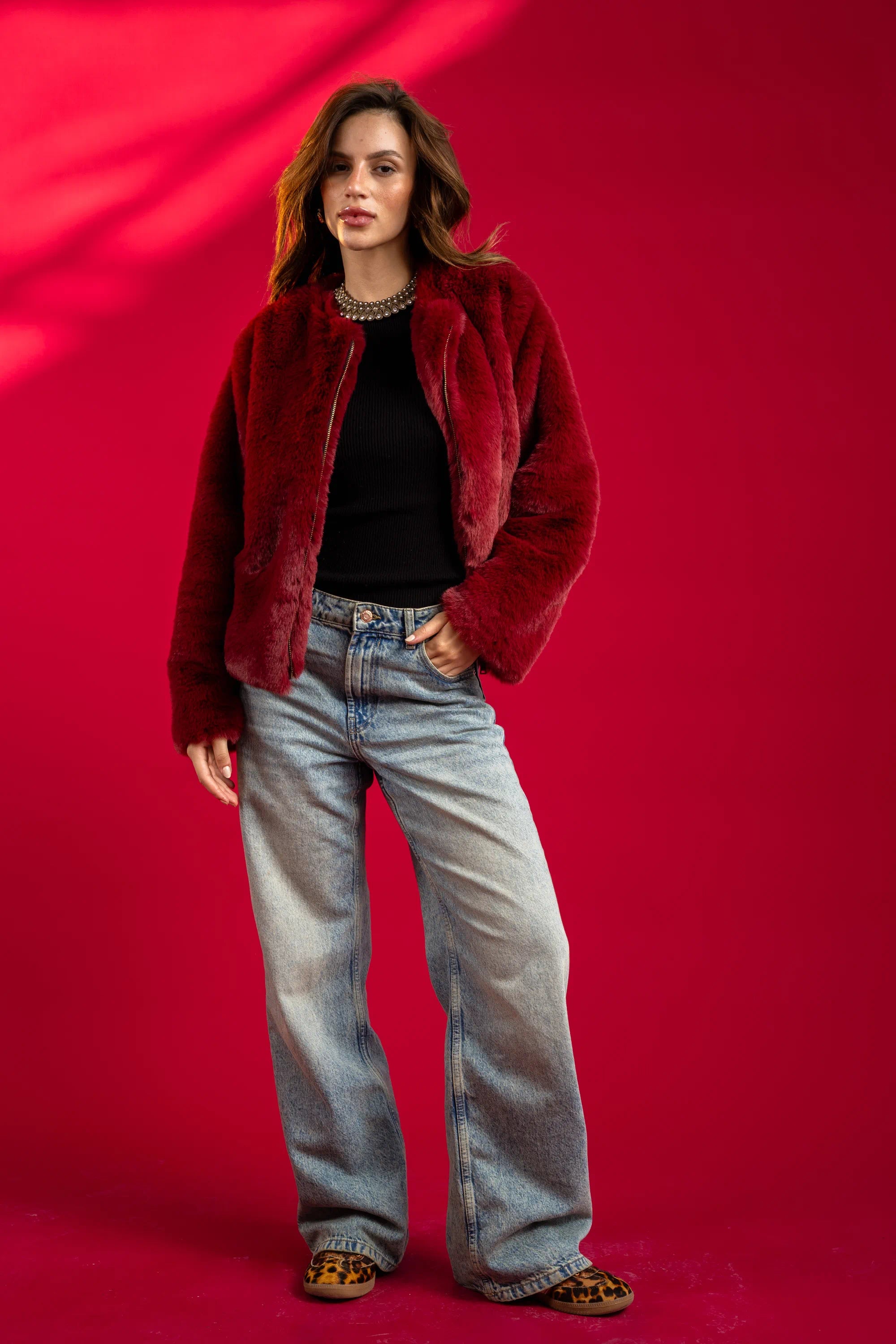 Woman wearing a red jacket and blue jeans against a red background