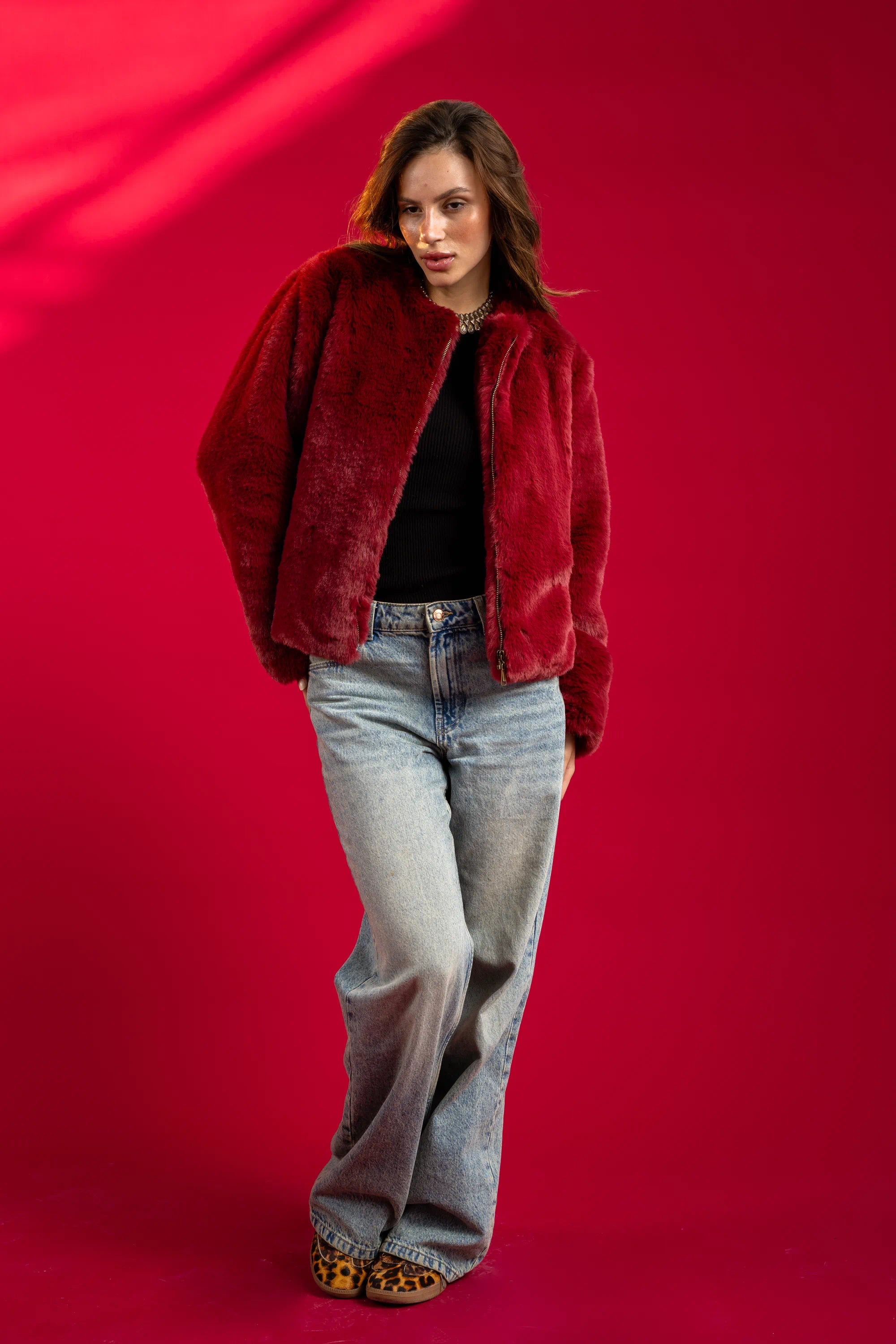 Person wearing a red fur coat and jeans on a red background