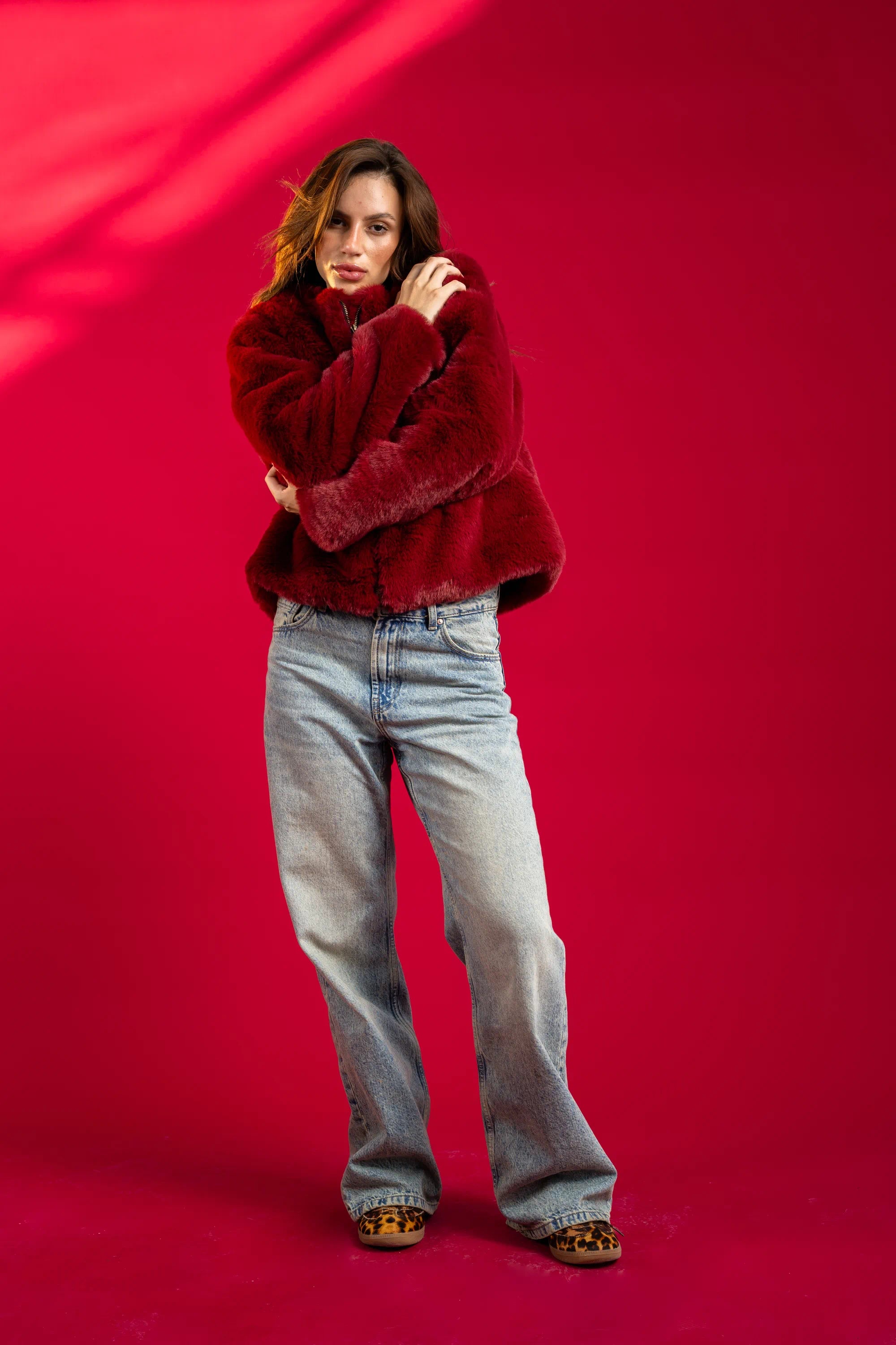 Woman wearing a red fur coat and jeans against a red background