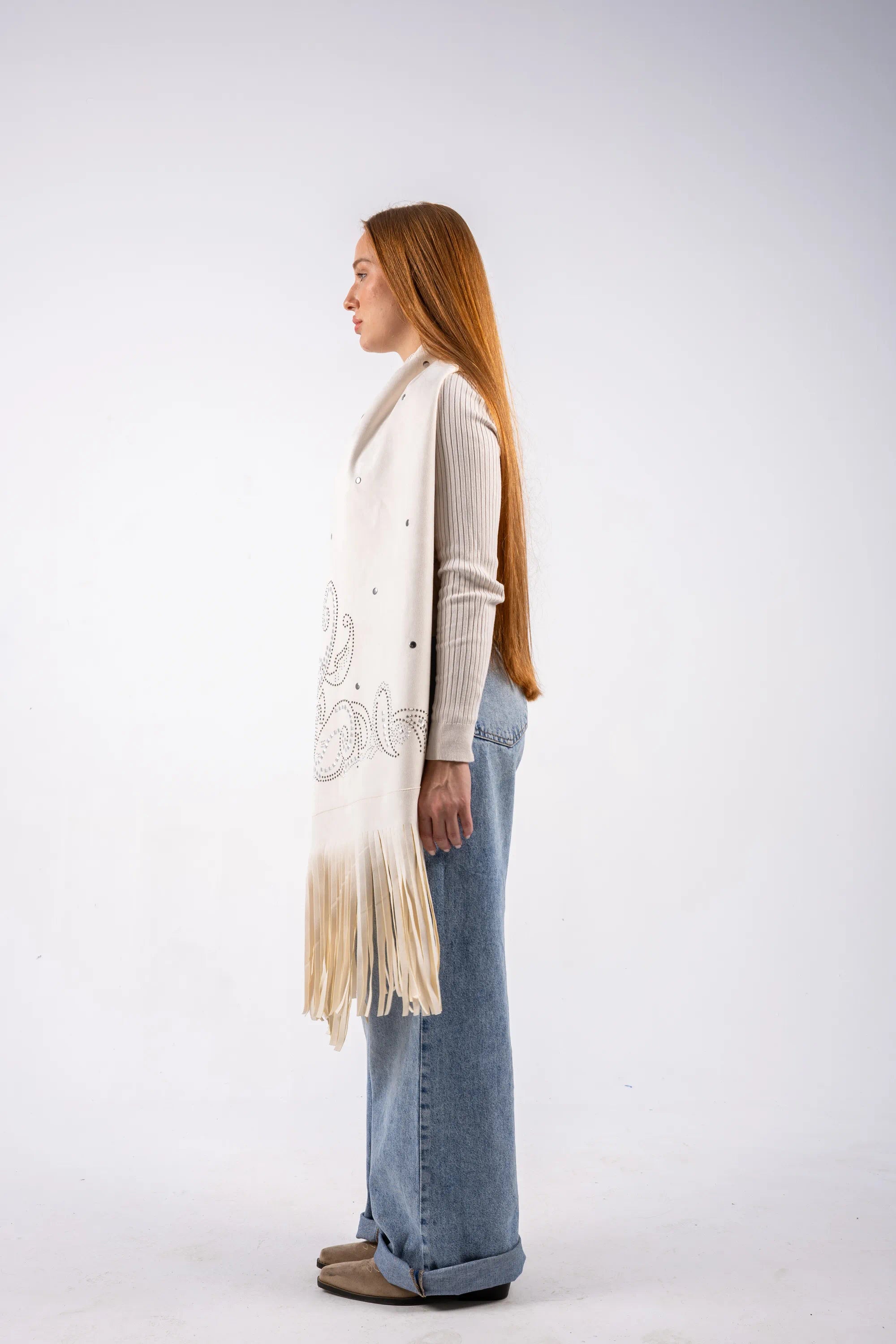 Woman wearing a long beige cardigan with fringe, standing against a white background