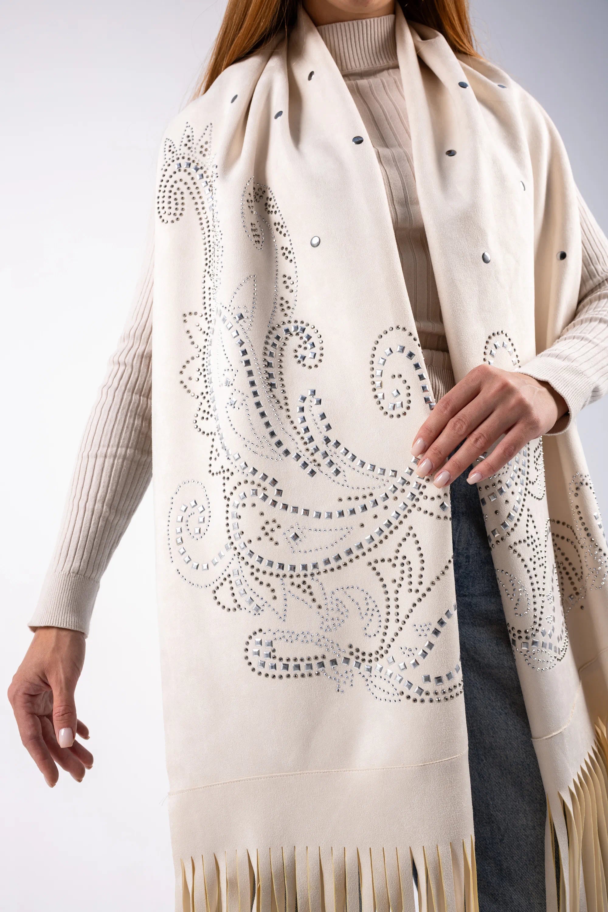 Beige scarf with intricate patterns and fringes worn by a person on a light gray background