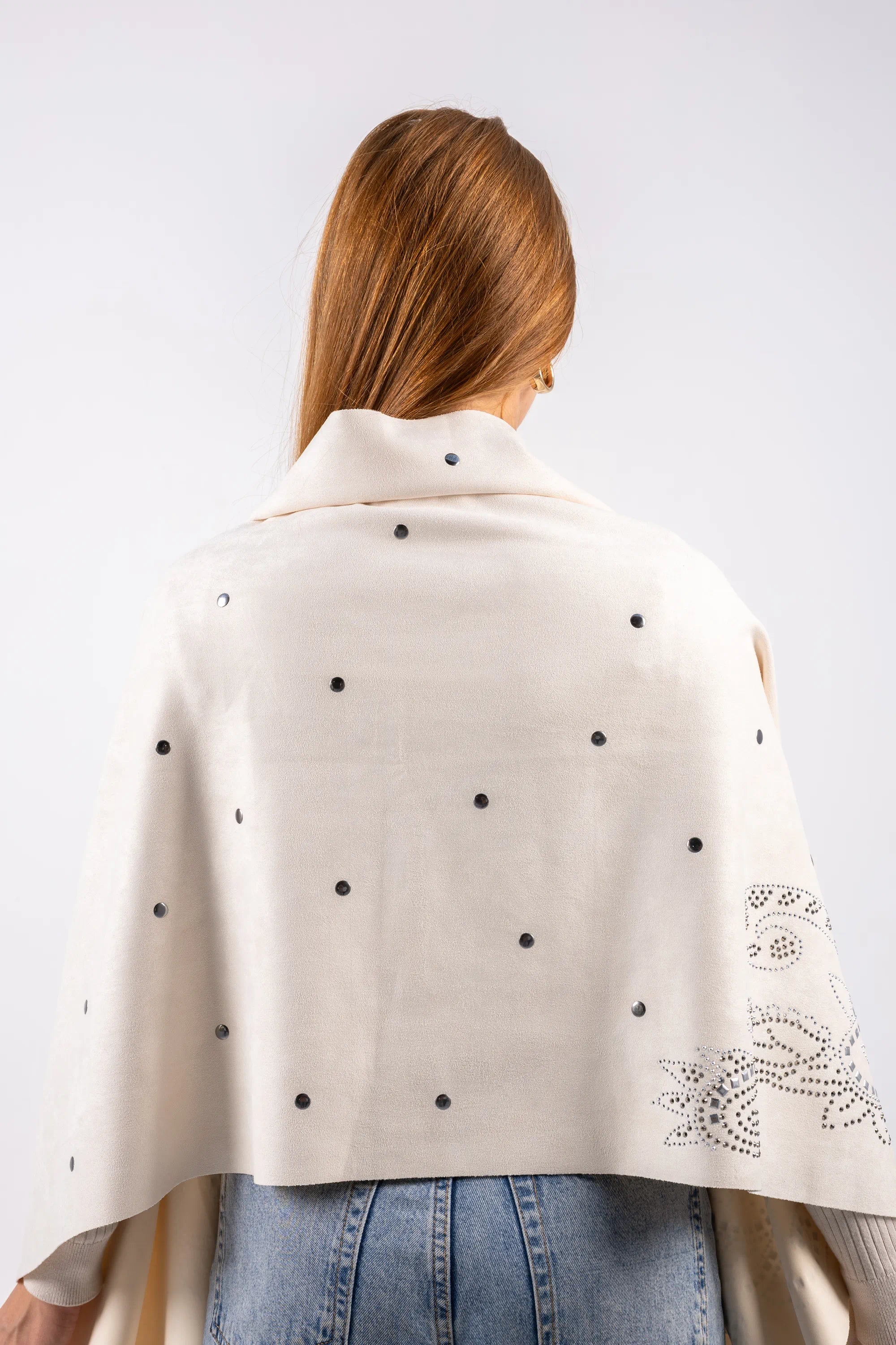 Woman wearing a cream-colored cape with black polka dots and floral embroidery on a white background
