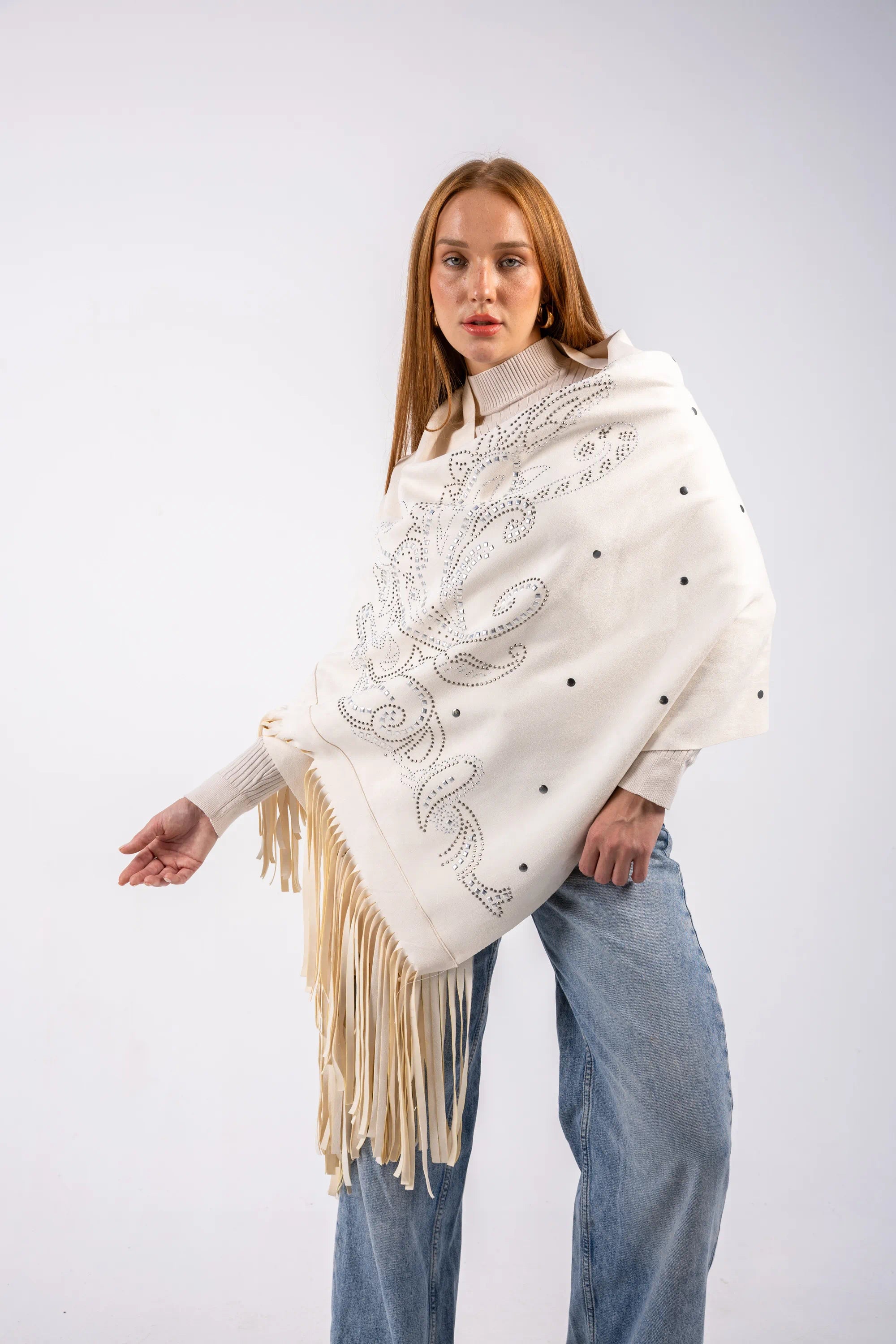 Woman wearing a white poncho with fringe and embroidery on a white background
