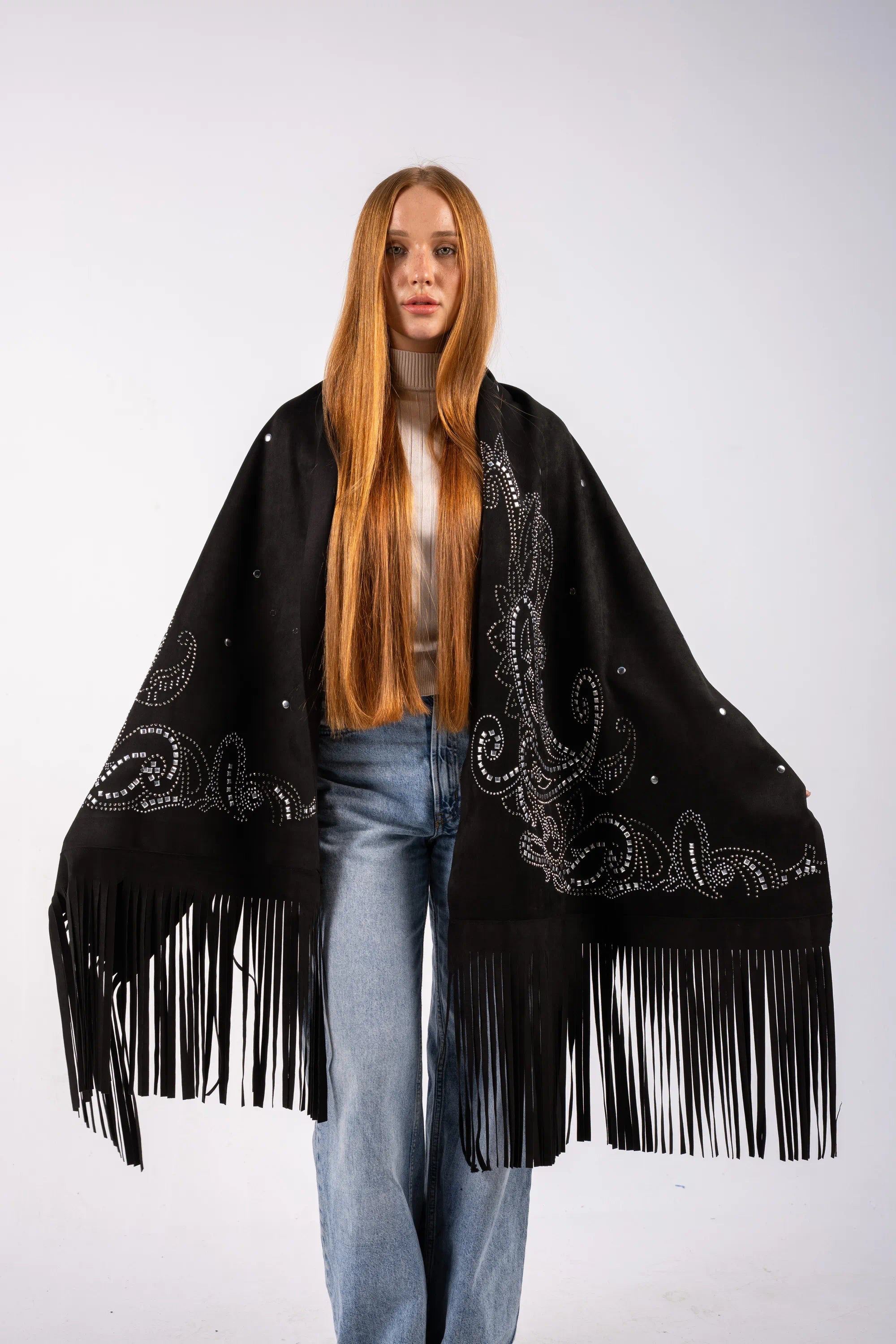 Person wearing a black fringed poncho with intricate designs on a white background