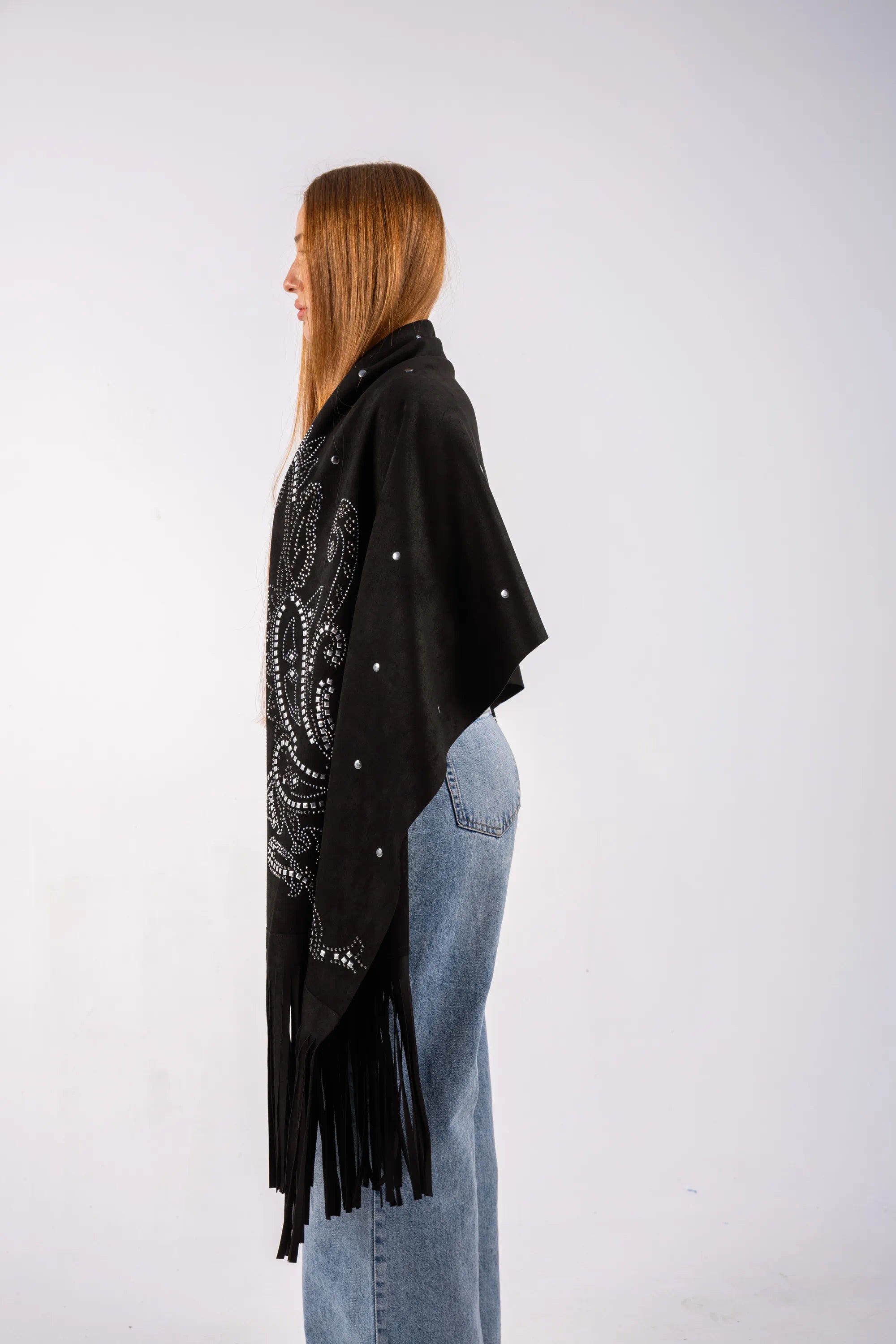 Woman wearing a black poncho with white patterns and fringes on a white background