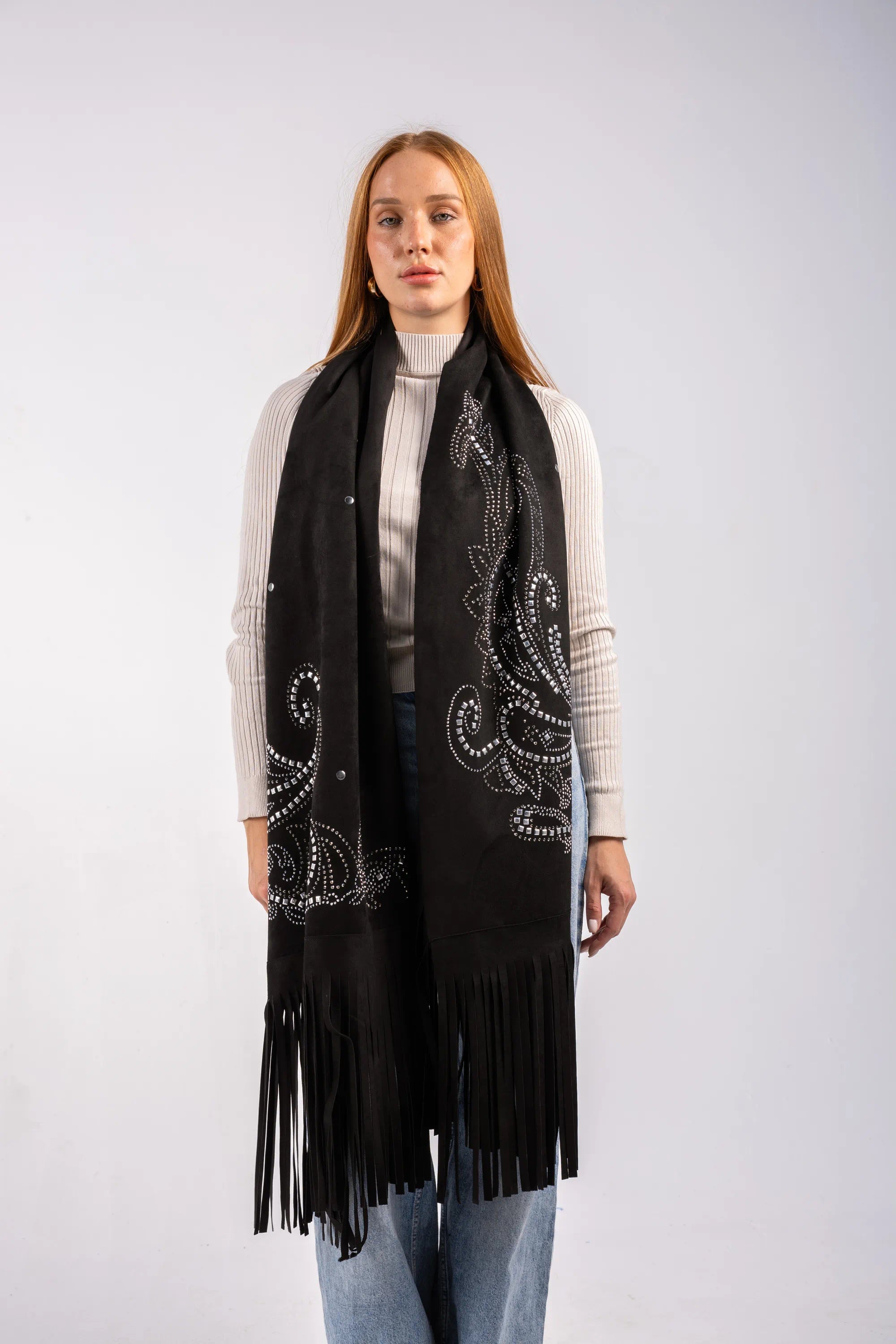Woman wearing a black scarf with white patterns and fringe on a plain background
