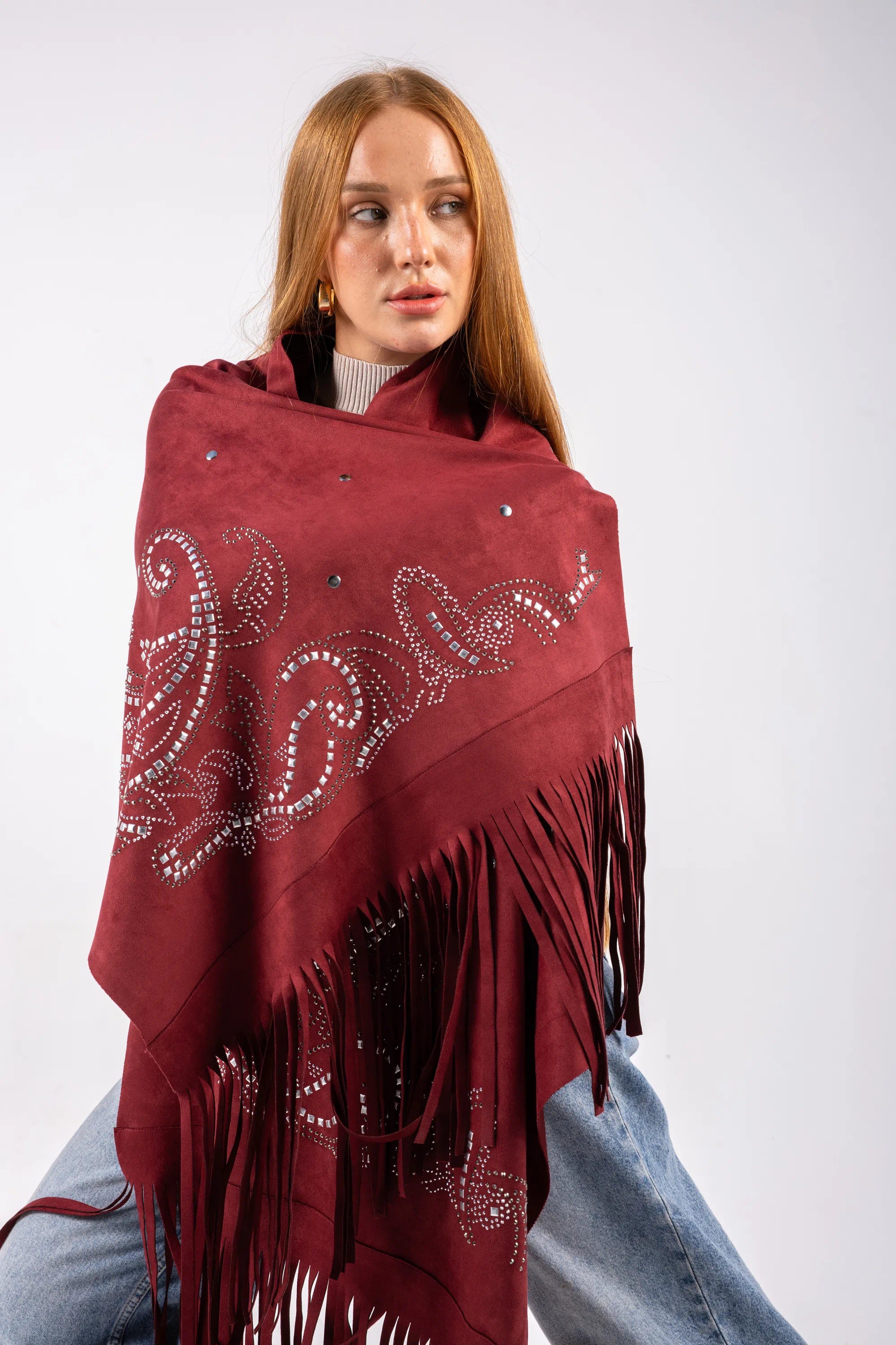 Woman wearing a burgundy shawl with white patterns and black fringe on a white background