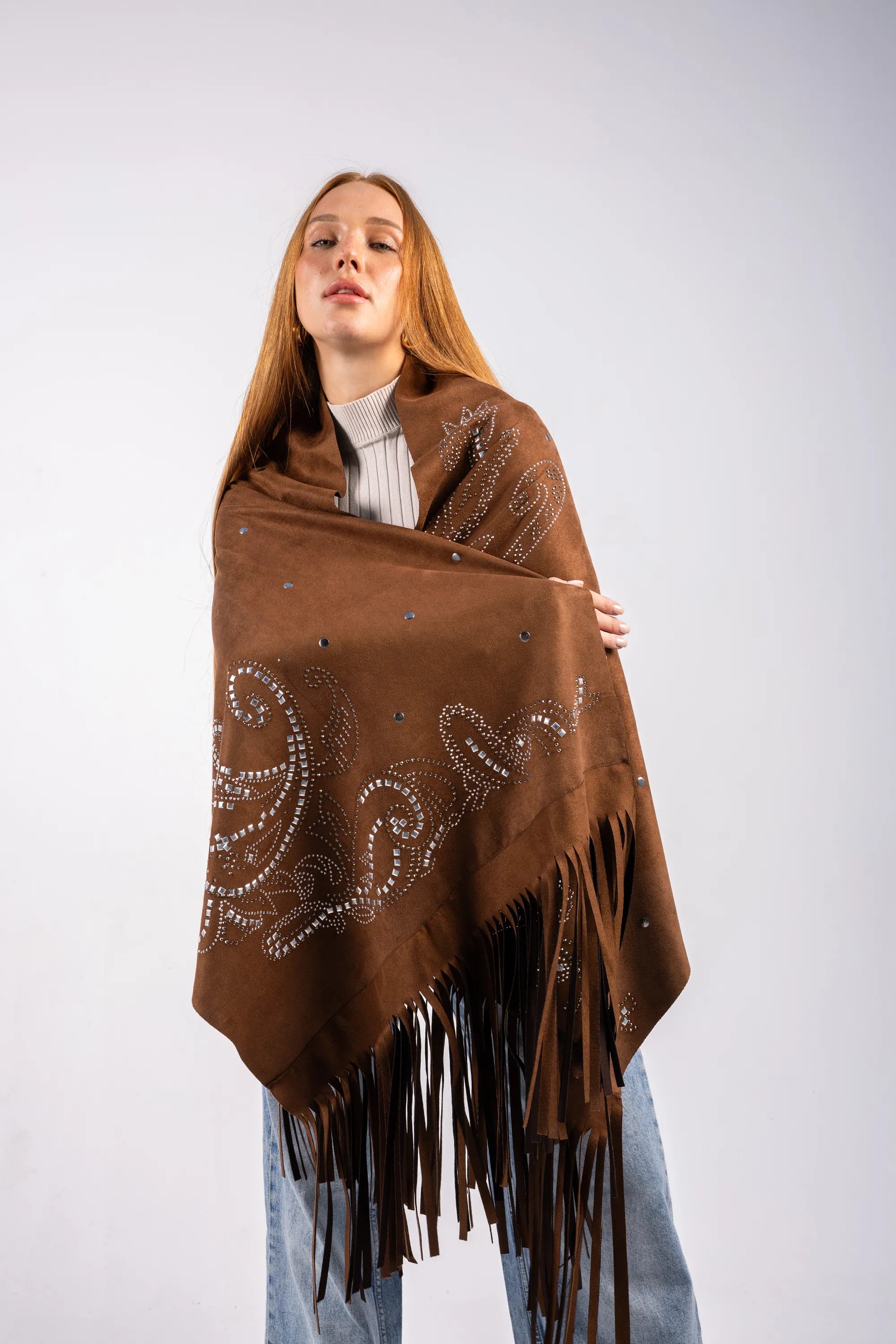 Woman wearing a brown poncho with decorative patterns and fringes on a white background