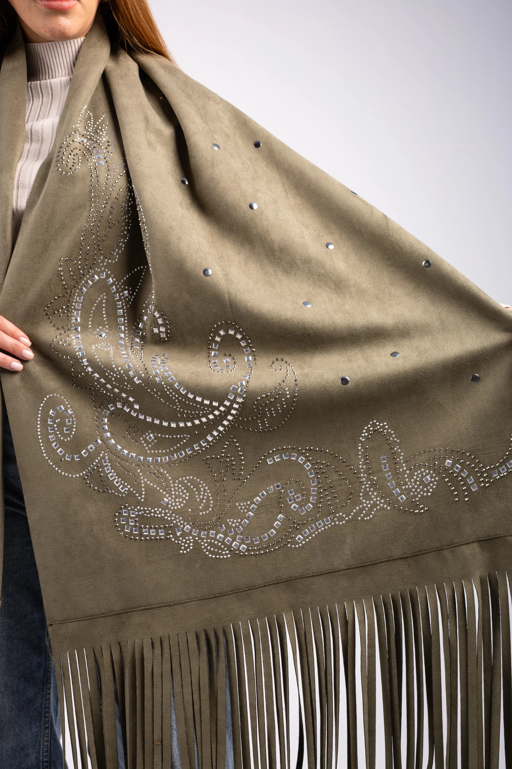 Green scarf with intricate white patterns and fringes held by a person against a neutral background