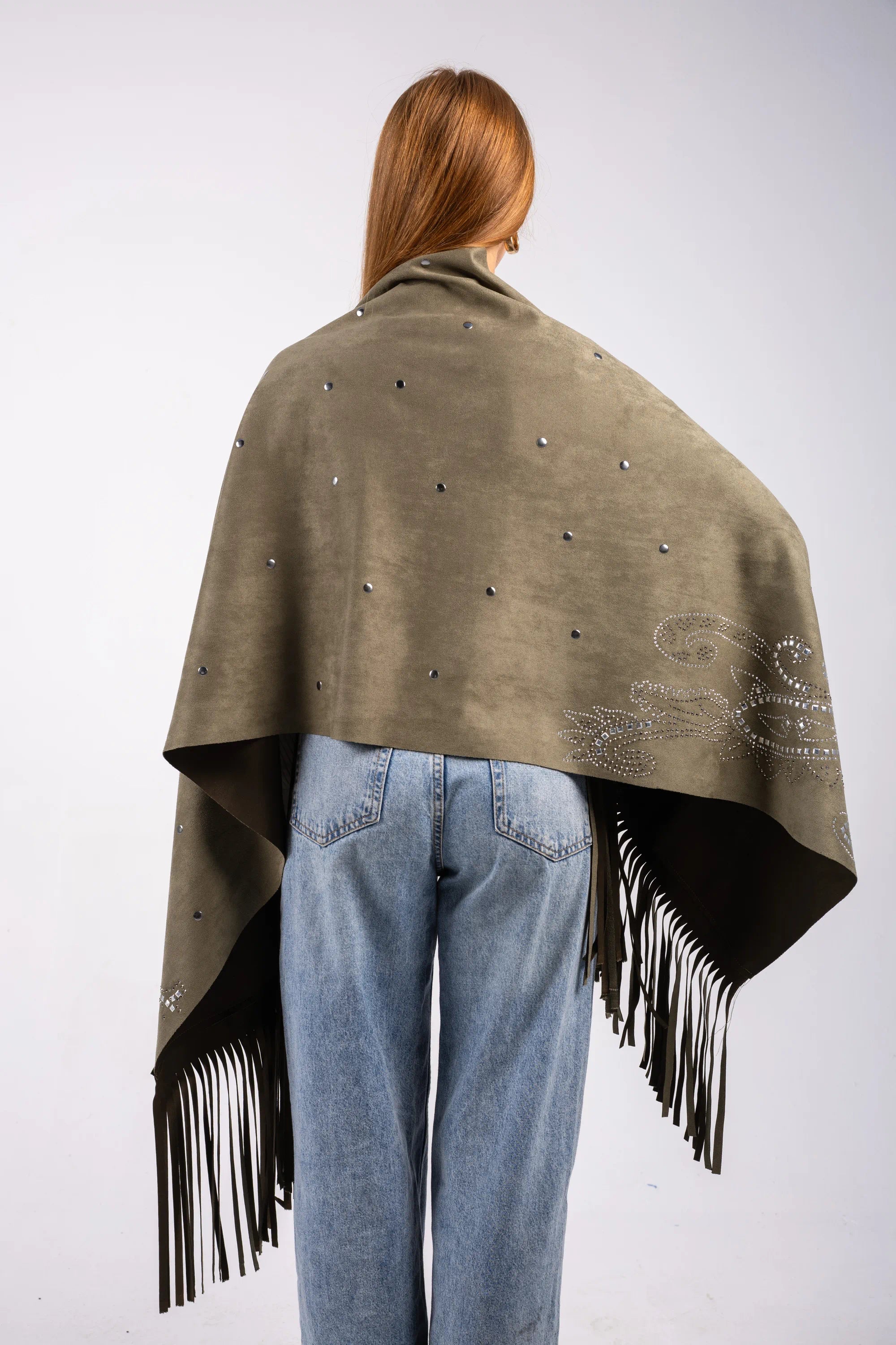 Person wearing a green poncho with black fringe and embellishments on a white background