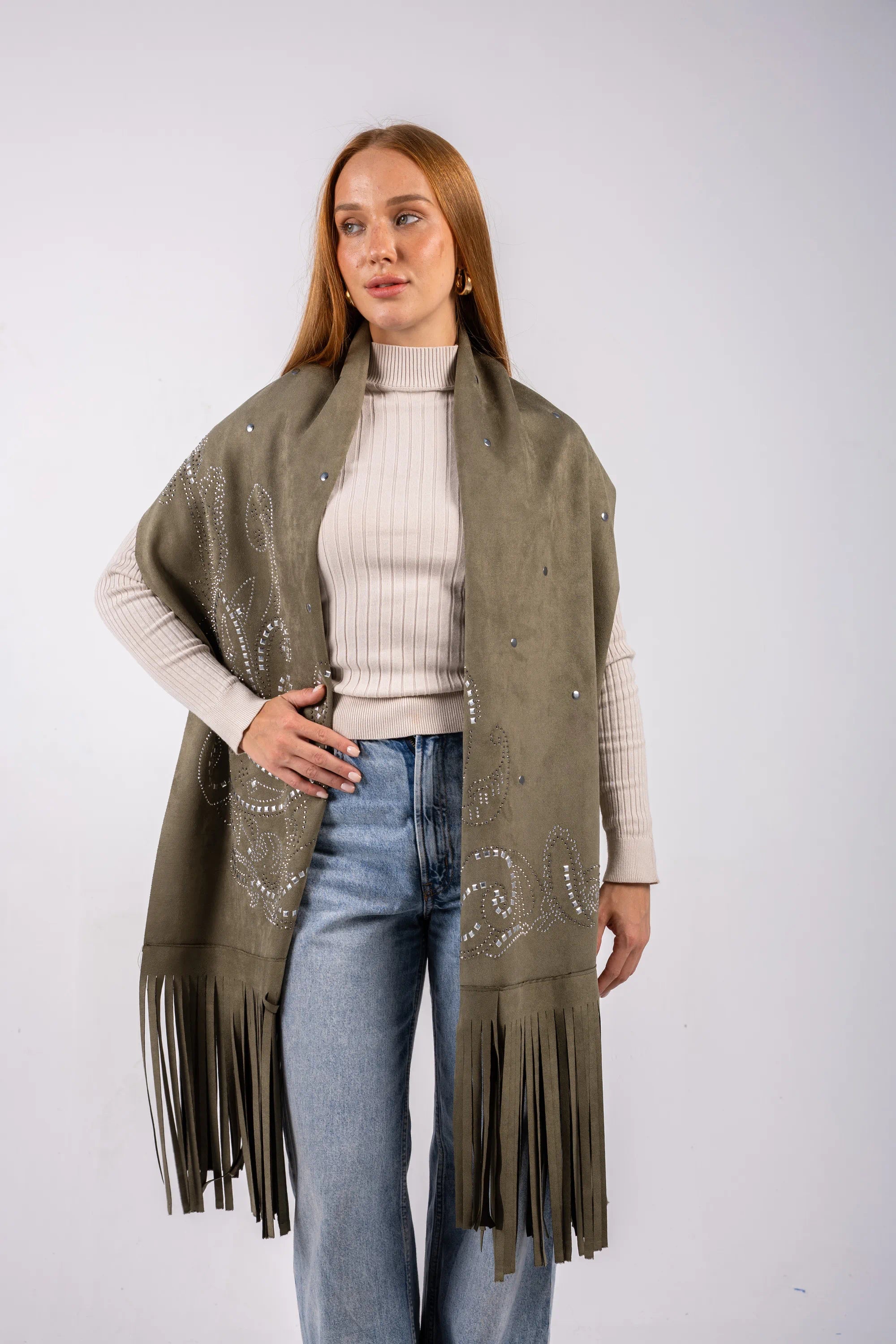Woman wearing a green fringe poncho over a white sweater and blue jeans on a white background