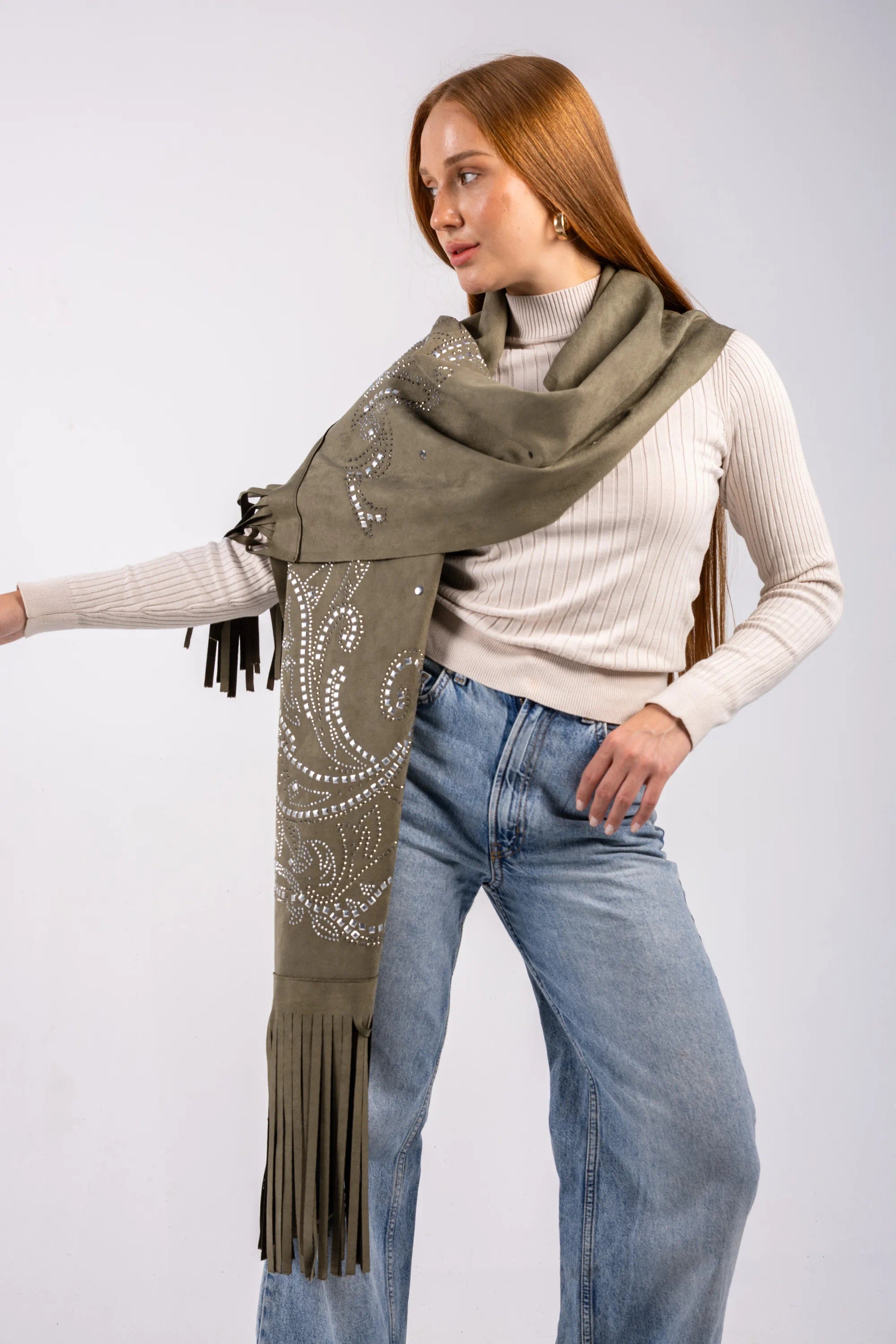 Woman wearing a green scarf with fringe and patterns, standing against a plain background