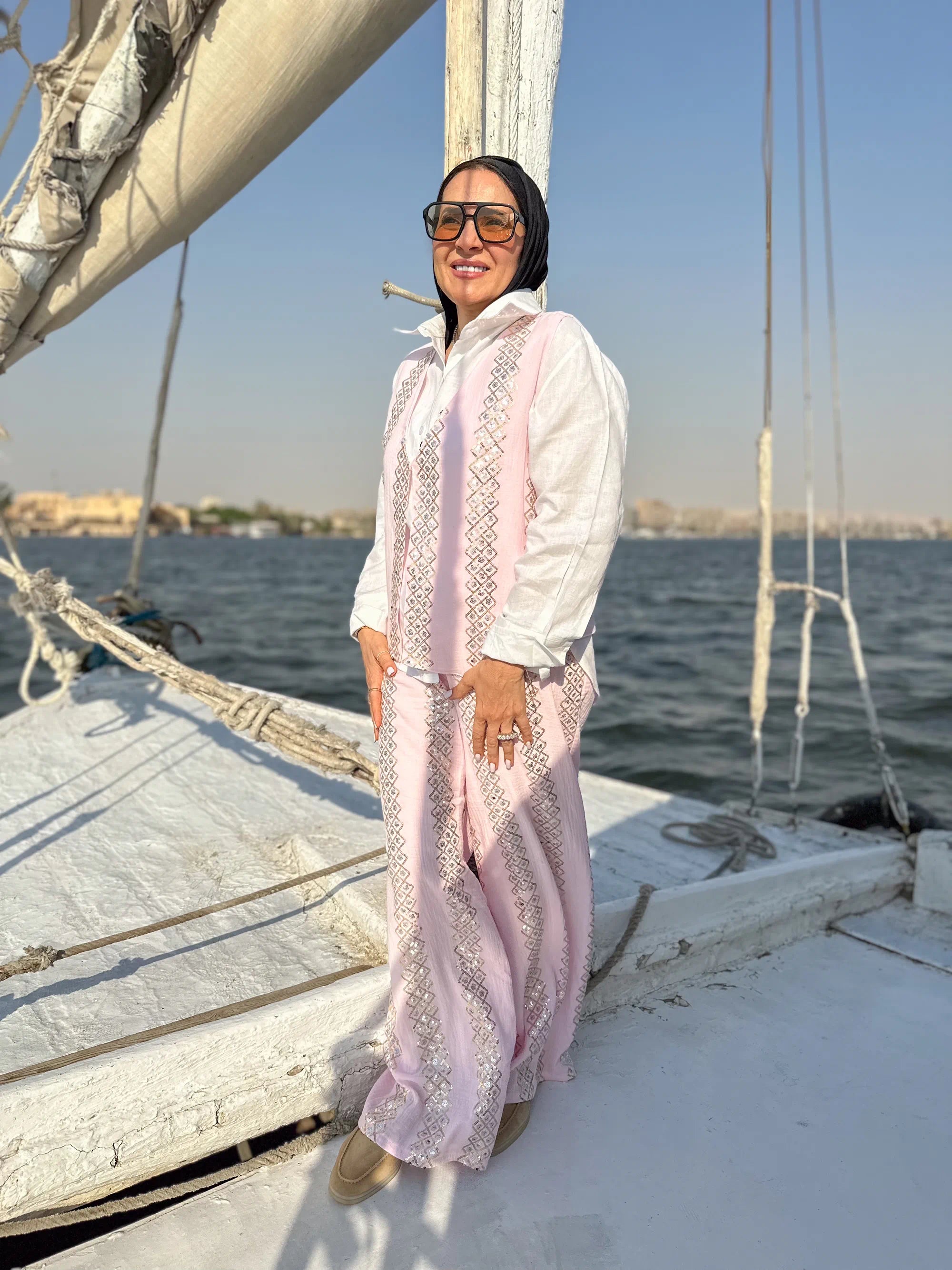 Woman in a white and pink outfit standing on a sailboat with water and sky in the background