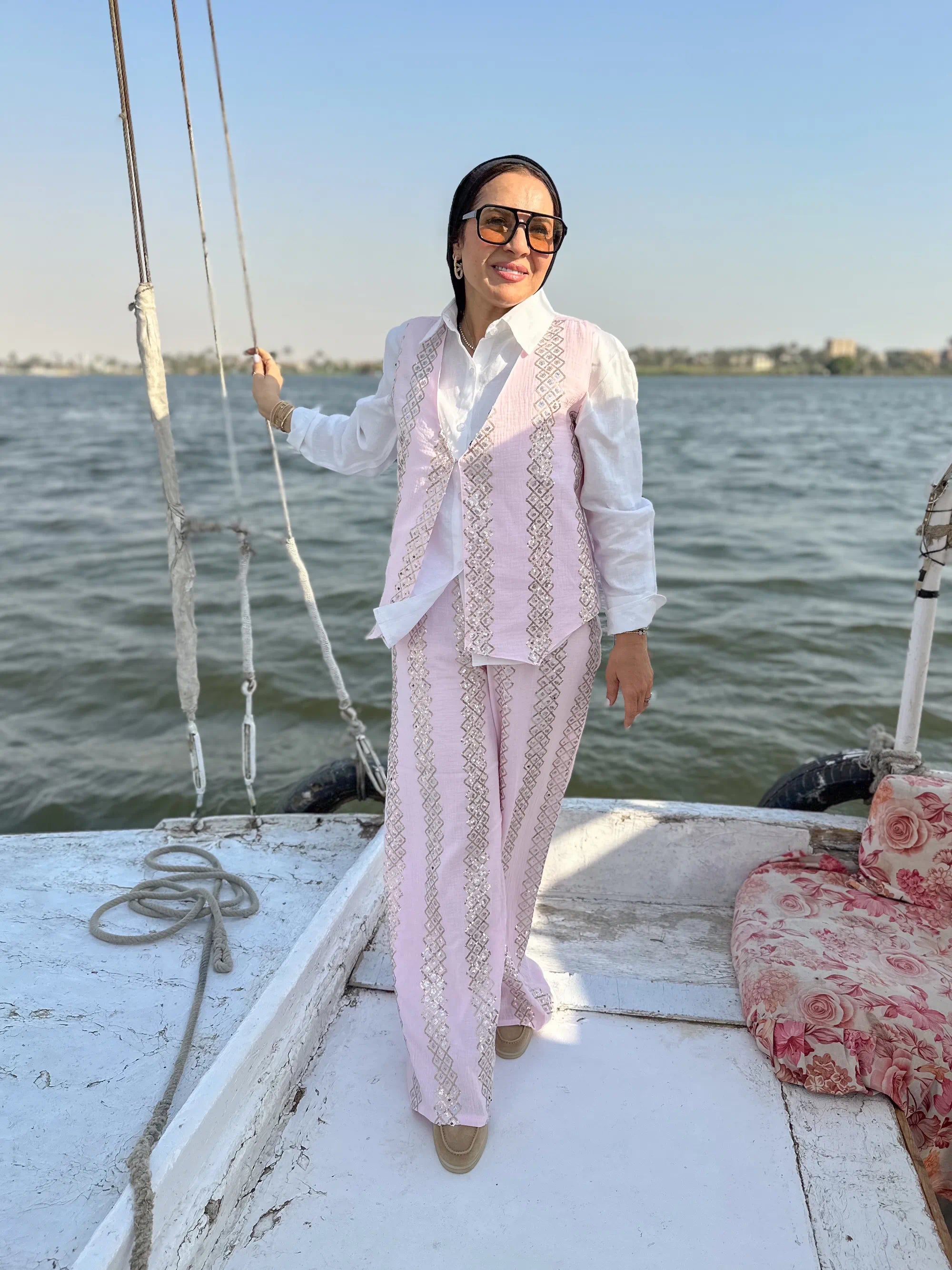 Woman in a light pink traditional outfit standing on a boat by a body of water.