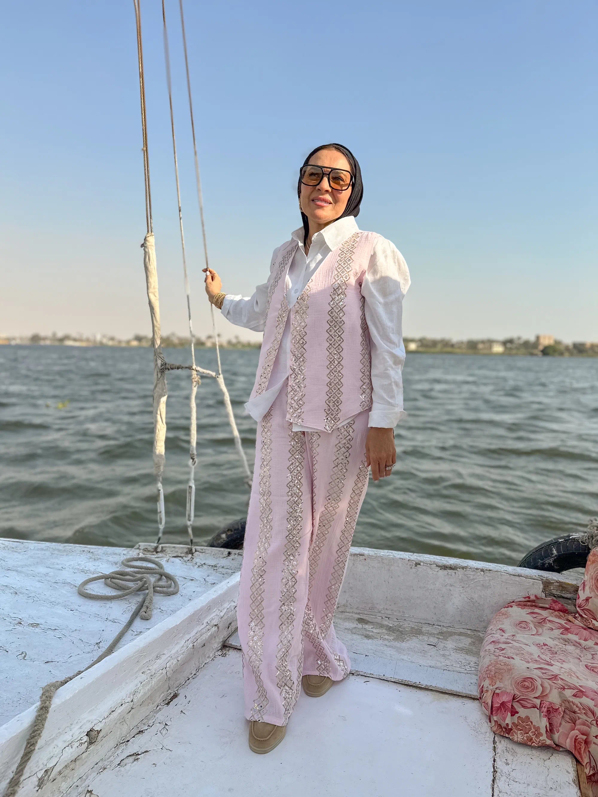 Person in a pink and white outfit standing on a boat with water and sky in the background