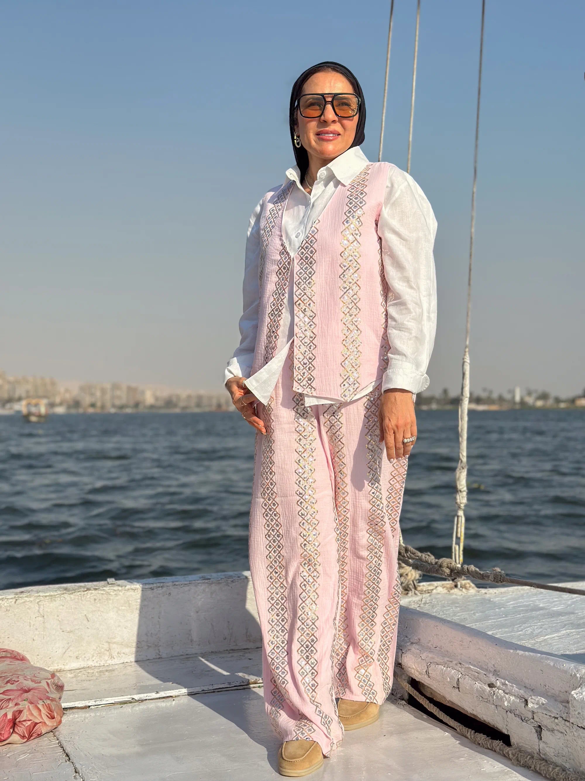 Woman in a pink traditional outfit standing on a boat with water and skyline in the background