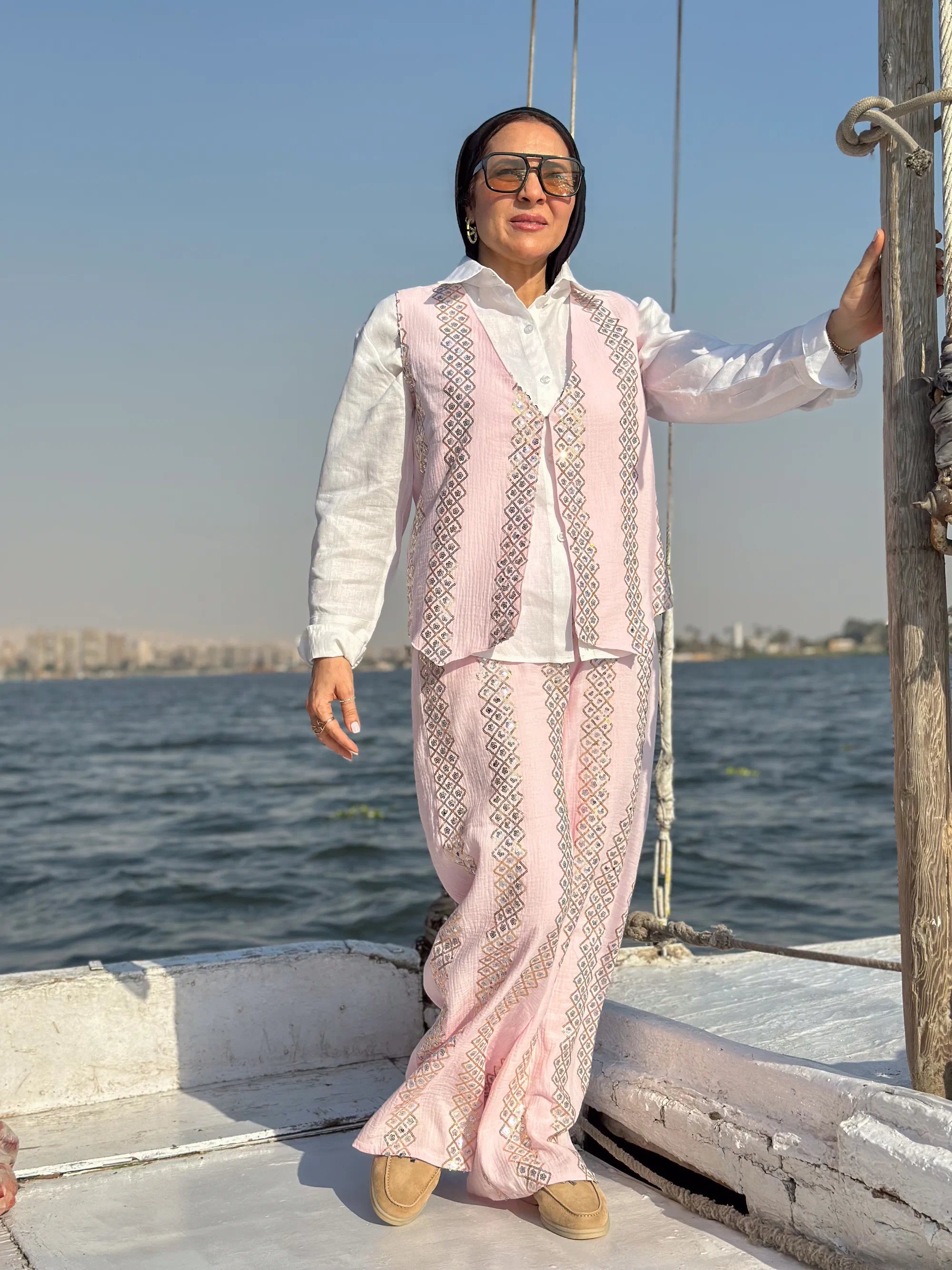 Woman in a light pink traditional outfit standing on a boat with water and skyline in the background