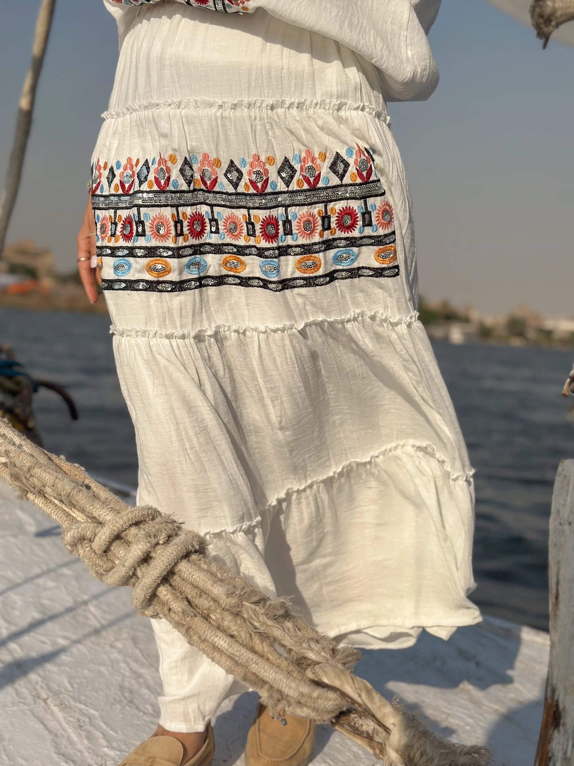 Person wearing a white dress with colorful patterns on a boat