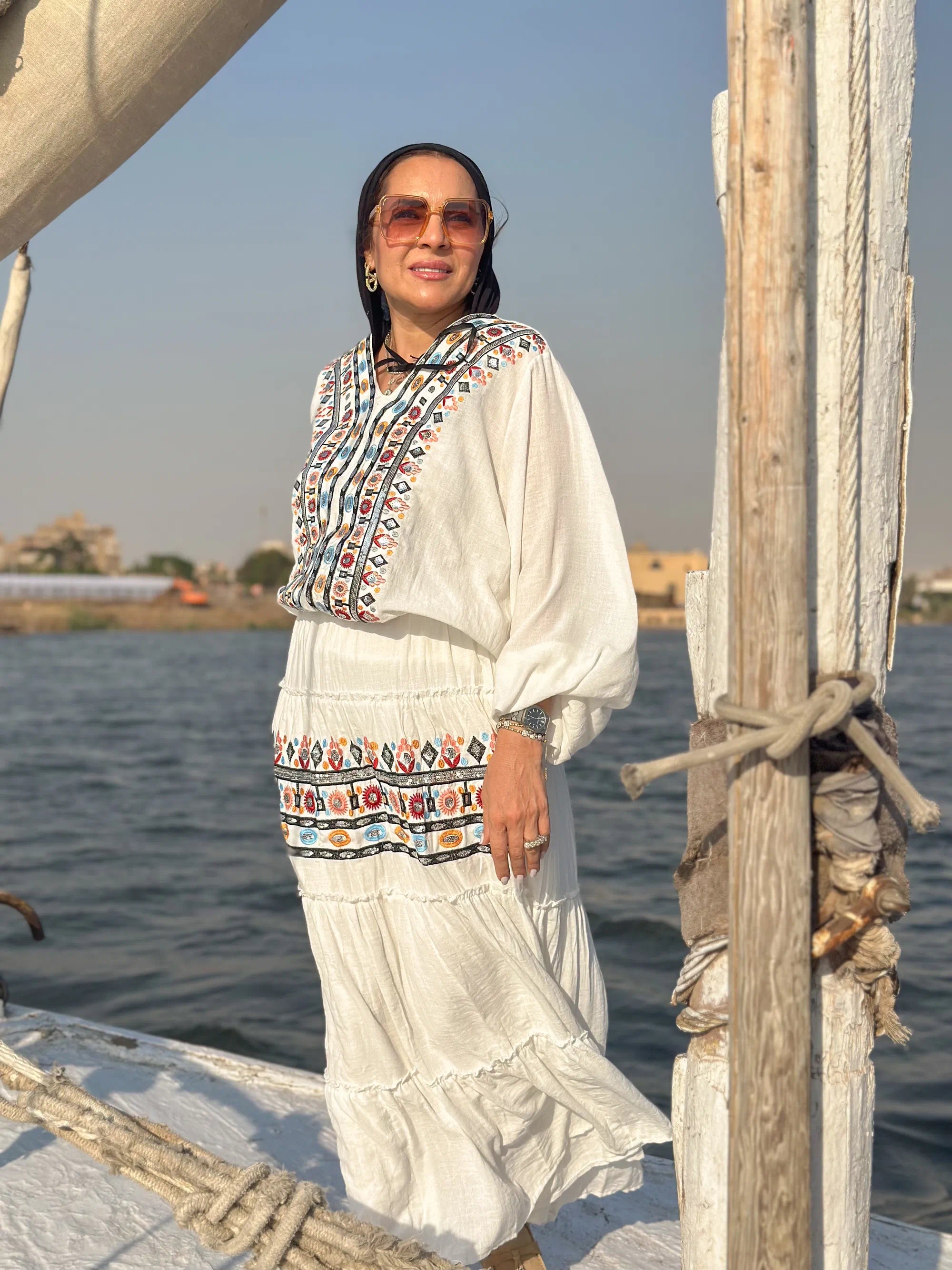 Woman in traditional attire standing on a boat with water and sky in the background