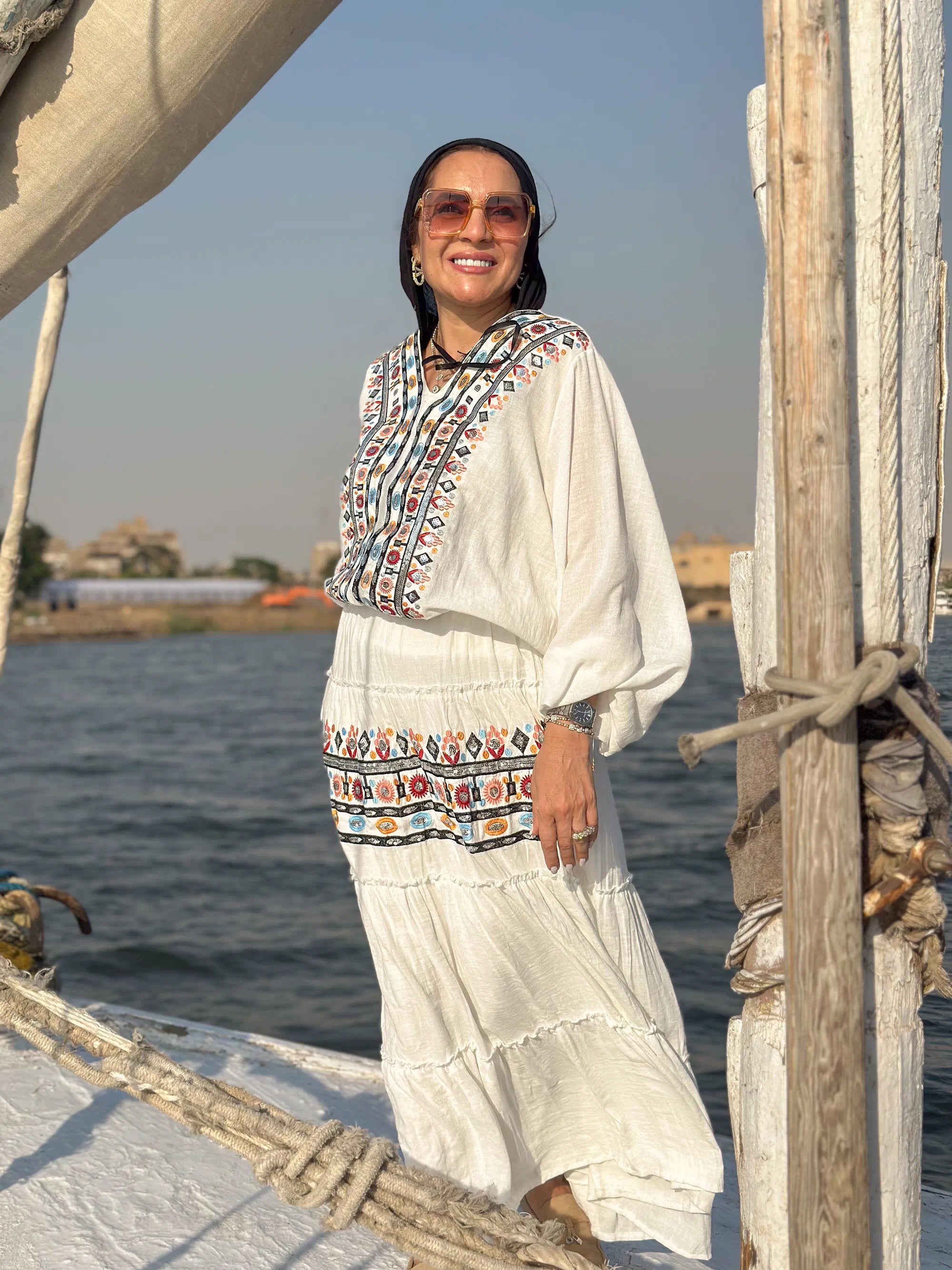 Woman in traditional attire standing on a boat with water and sky in the background