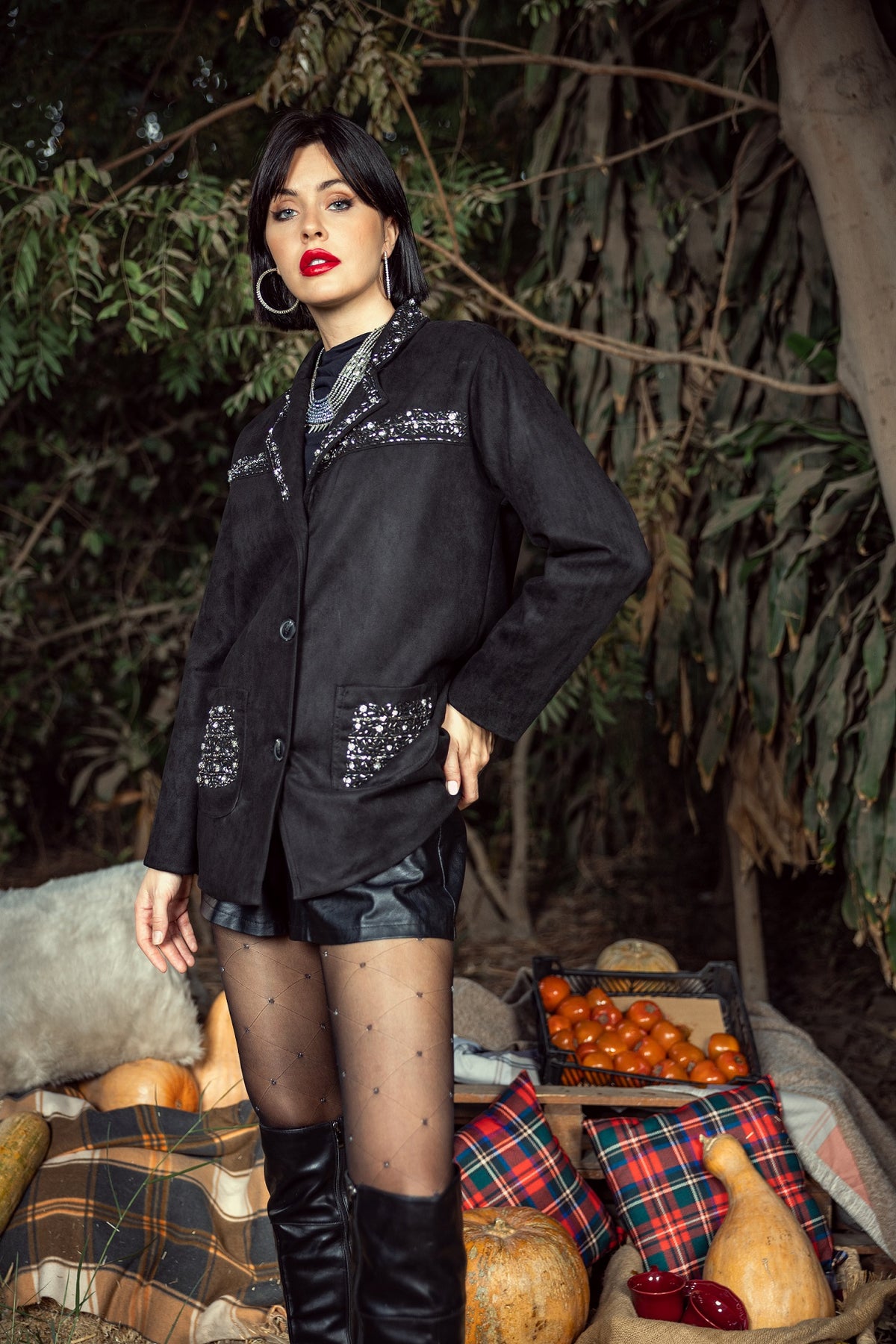 Woman in a black sequined jacket standing outdoors with pumpkins and a plaid blanket.