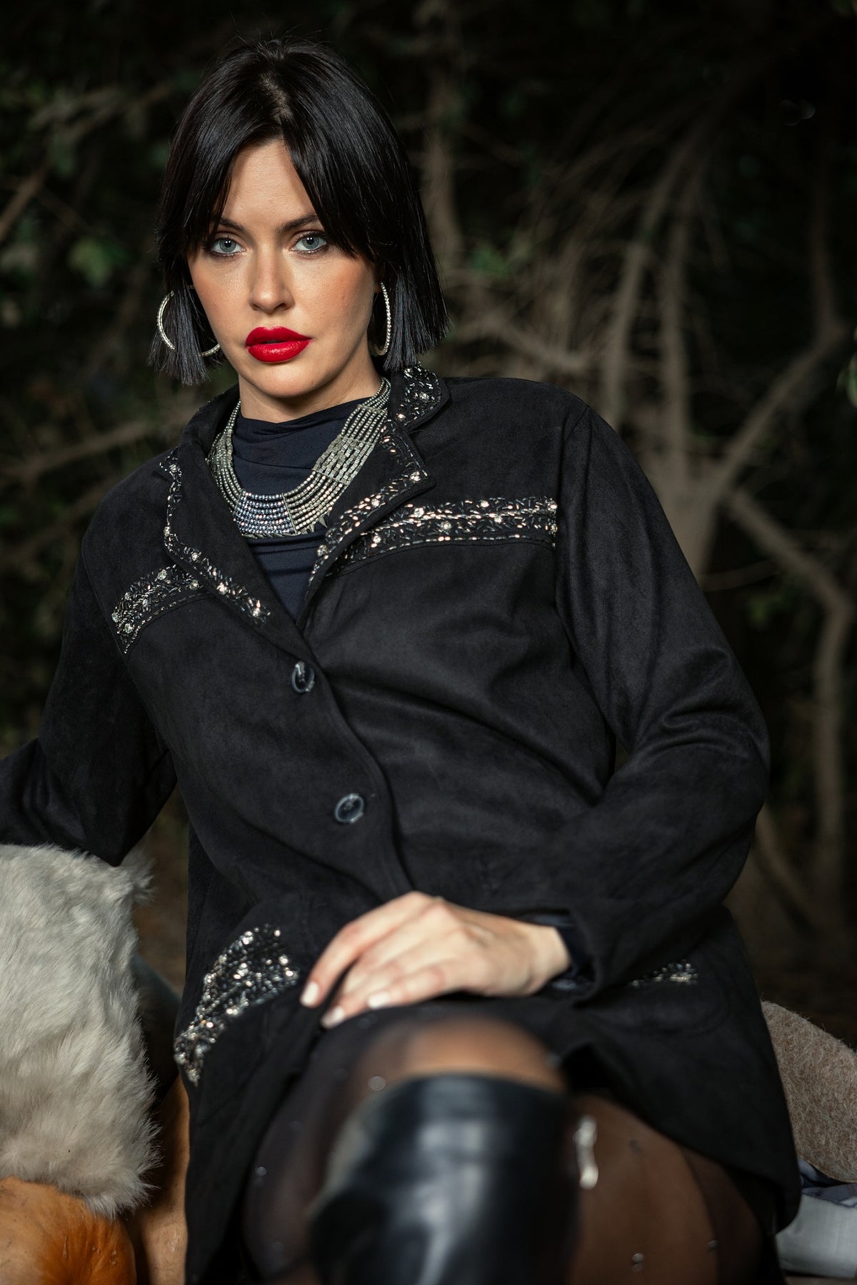 Woman wearing a black coat with silver embellishments sitting outdoors.