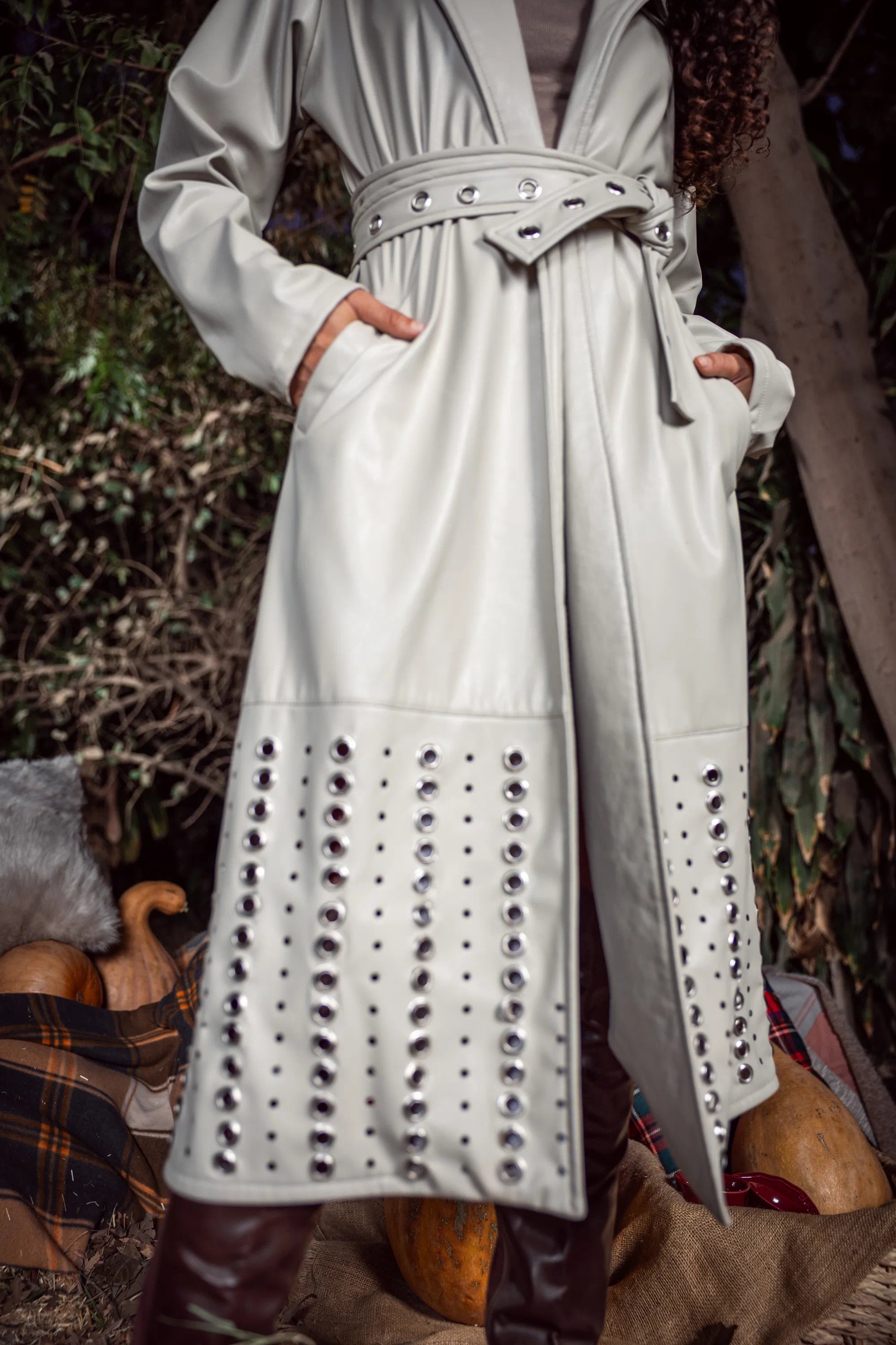 White leather coat with studded details worn by a person in an outdoor setting.