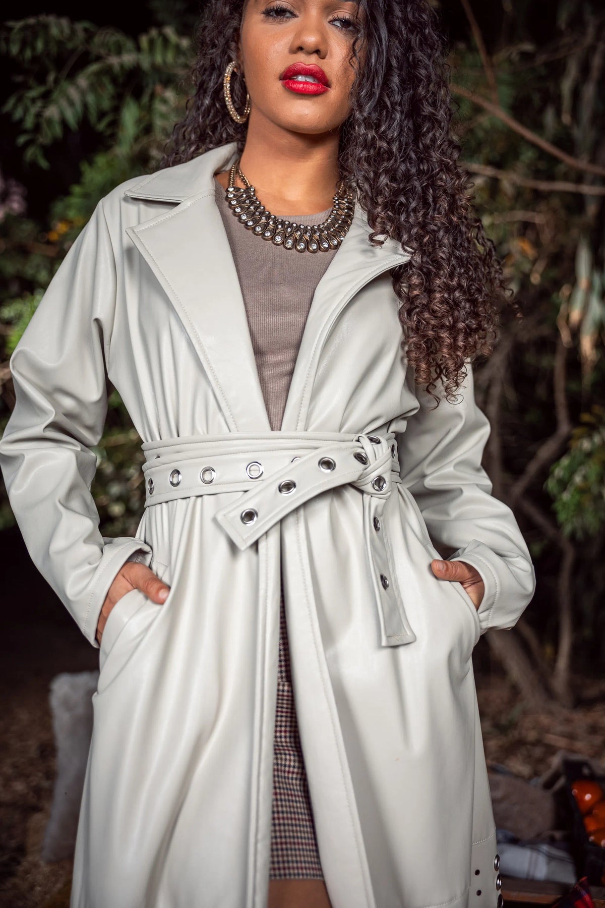 Woman wearing a light gray trench coat with a belt, standing outdoors.