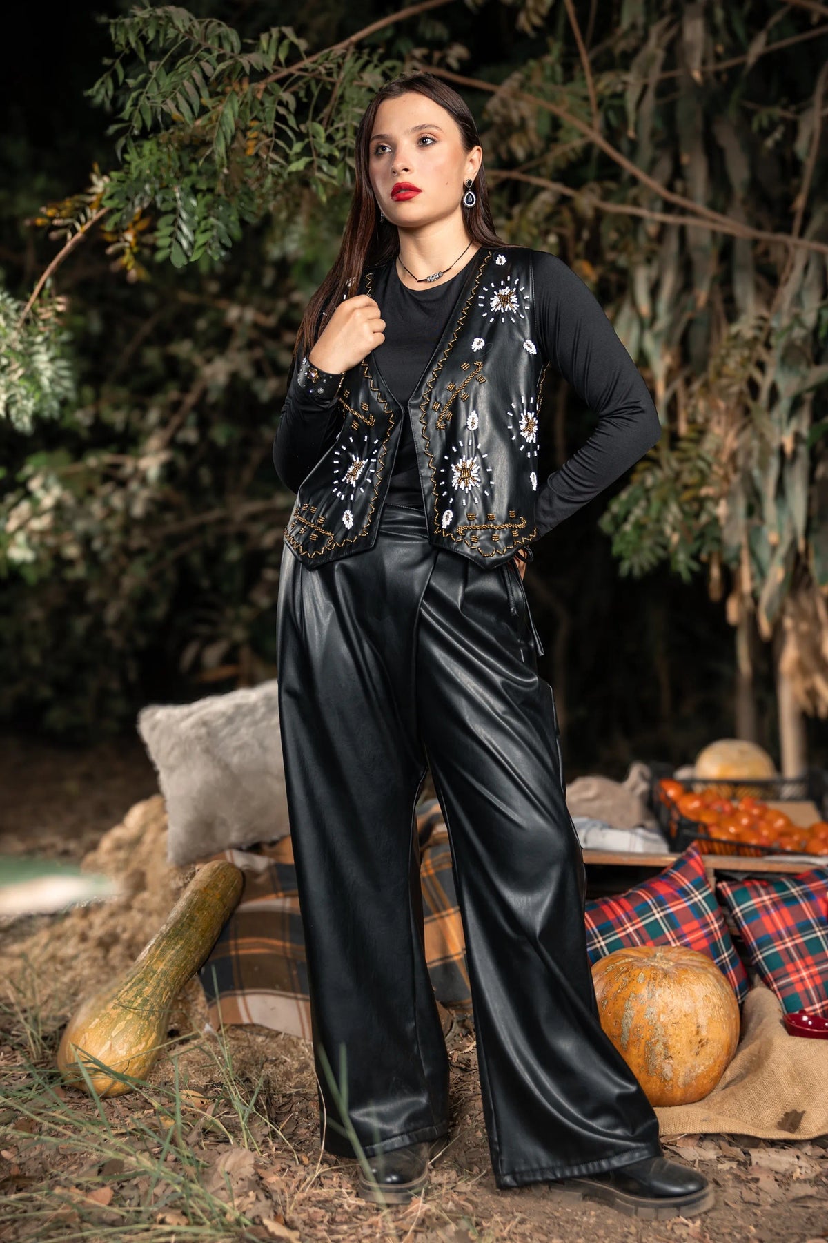 Woman in black outfit with floral details standing outdoors with pumpkins and foliage.
