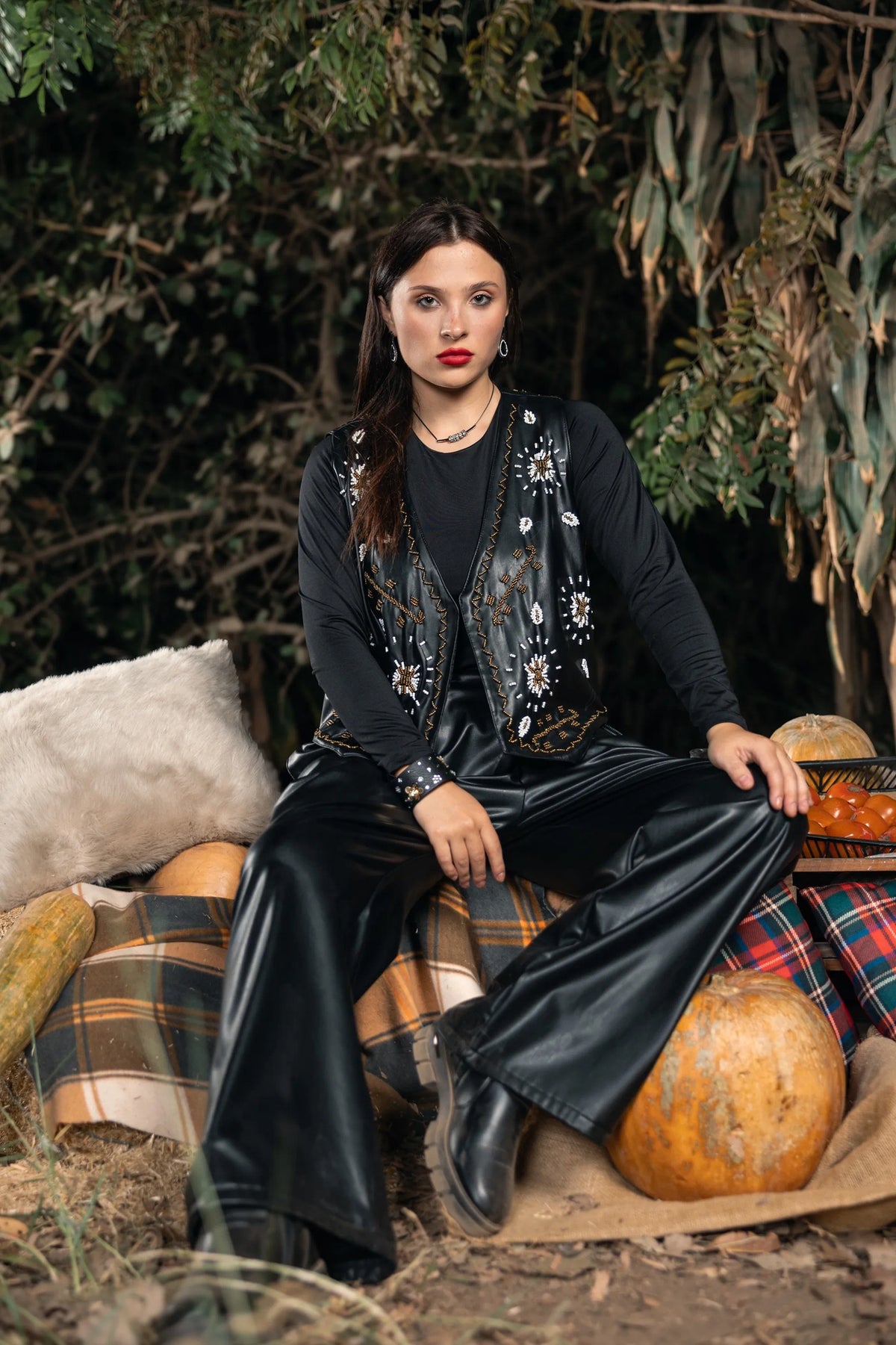 Woman in black outfit with embellishments sitting among pumpkins and autumn leaves.