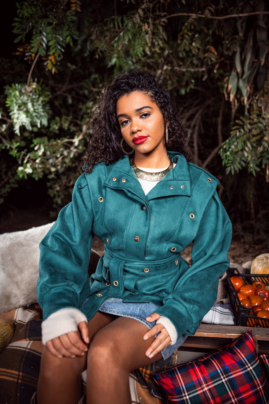 Woman in a teal coat sitting outdoors with greenery in the background