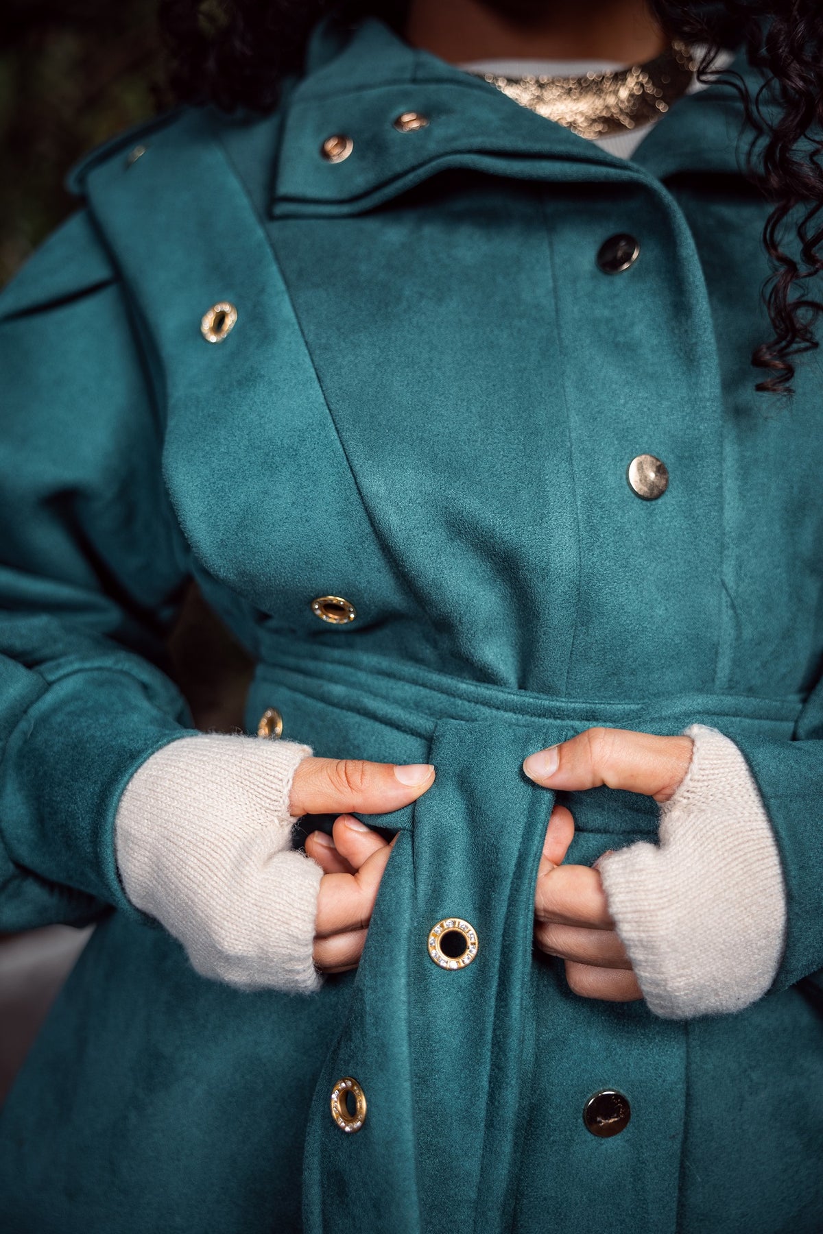 Teal coat with gold buttons worn by a person, focusing on the coat and hands.