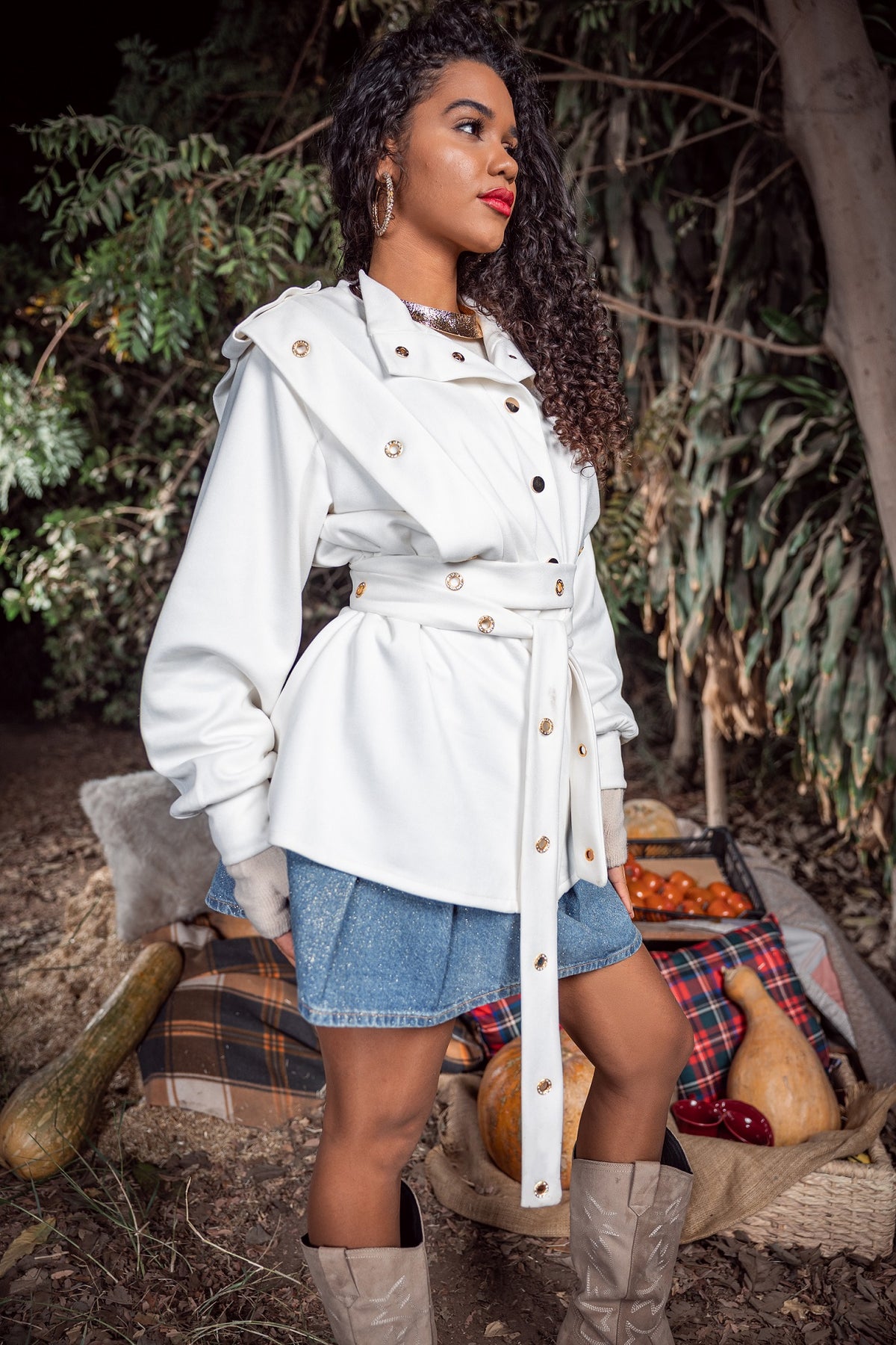 Woman wearing a white trench coat with a plaid blanket and pumpkins in the background
