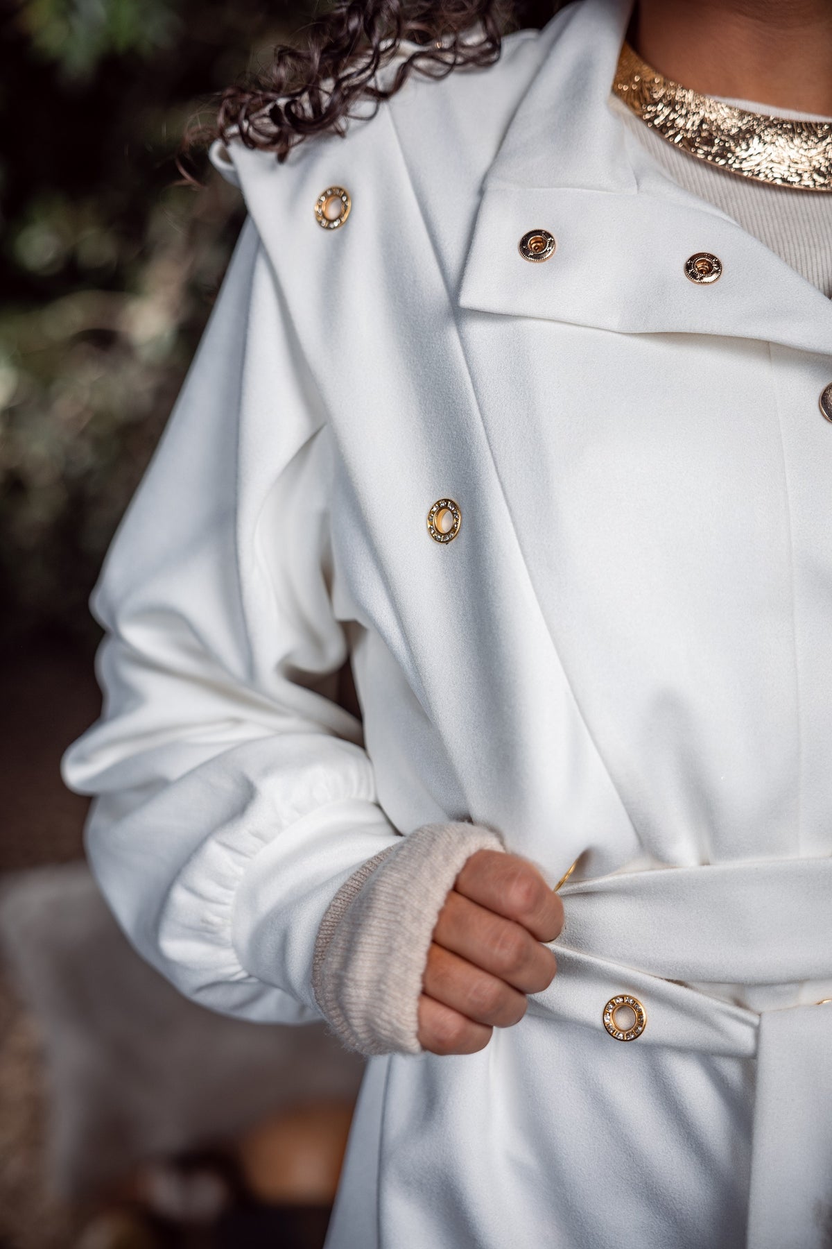Close-up of a person wearing a white coat with gold buttons against a blurred natural background
