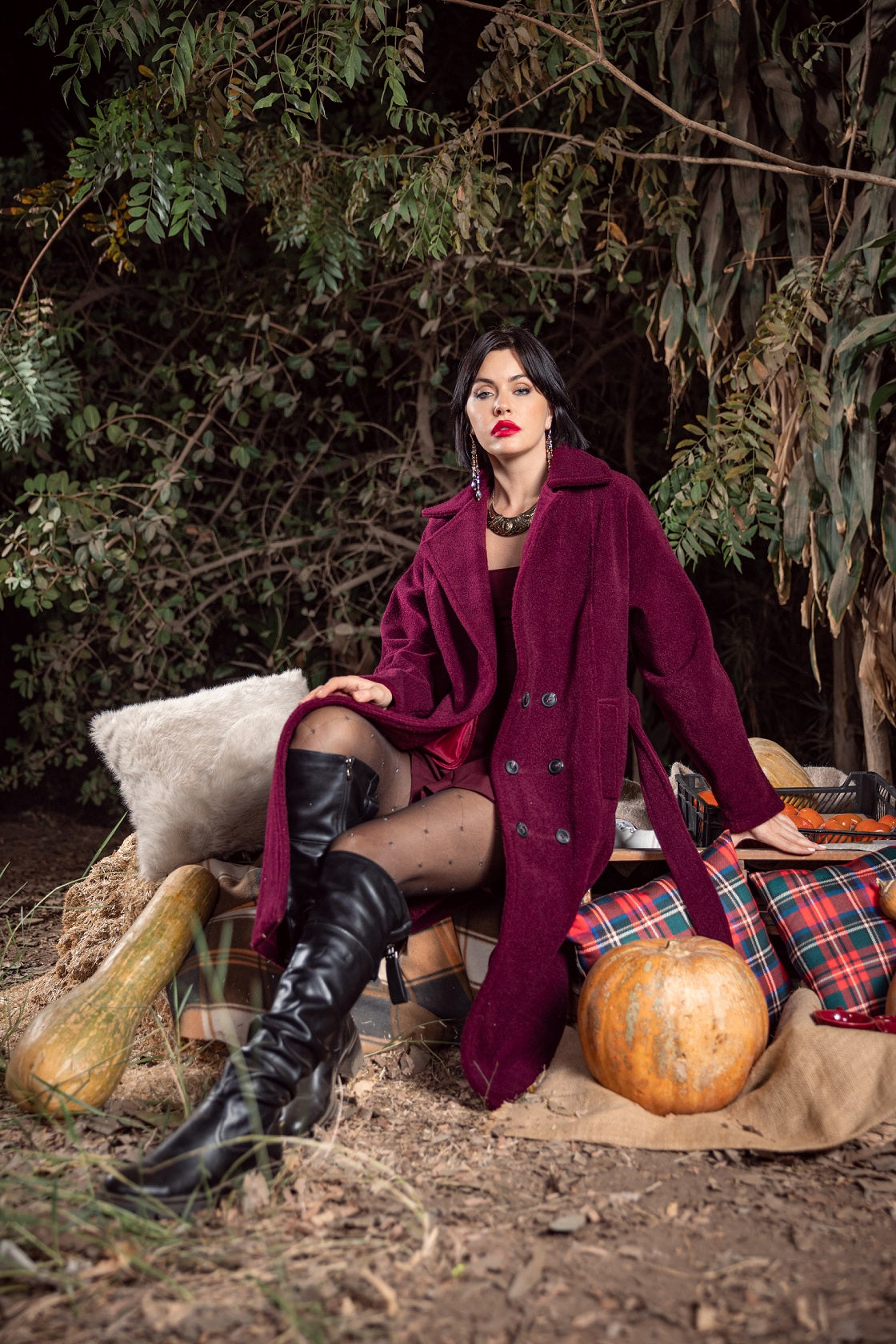 Woman in a purple coat sitting outdoors with pumpkins and plaid blanket