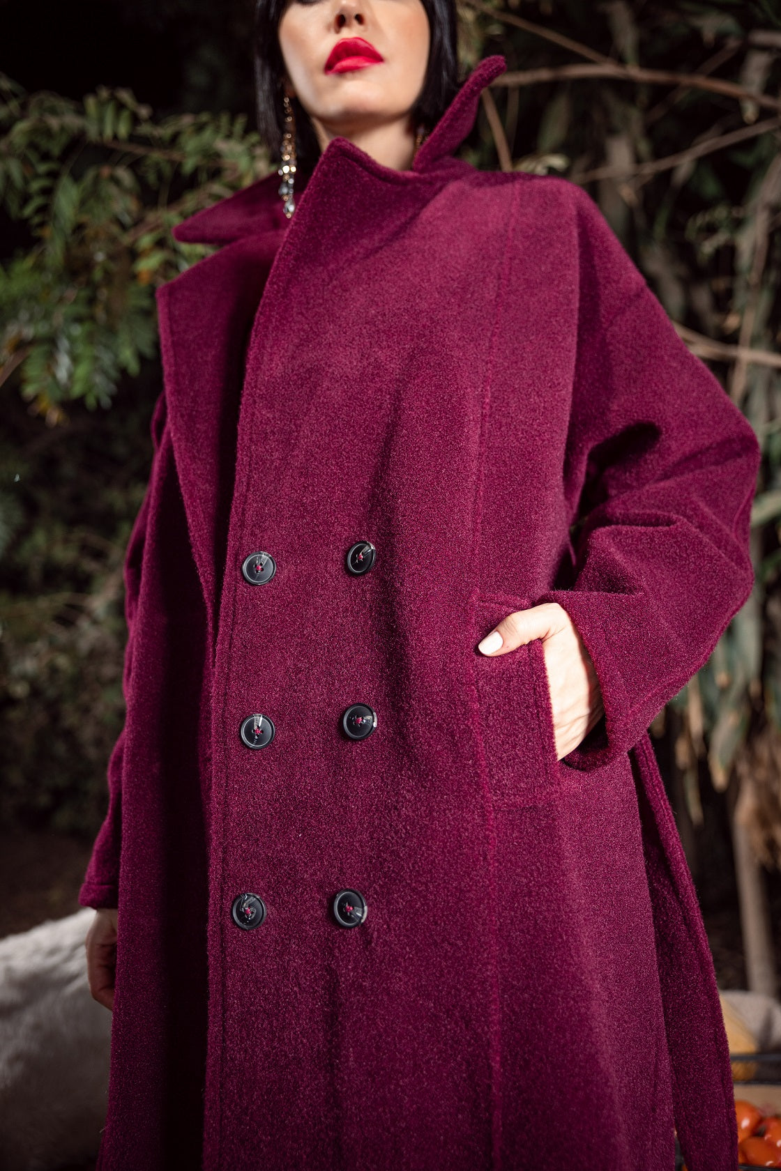 Person wearing a burgundy coat with black buttons against a blurred natural background