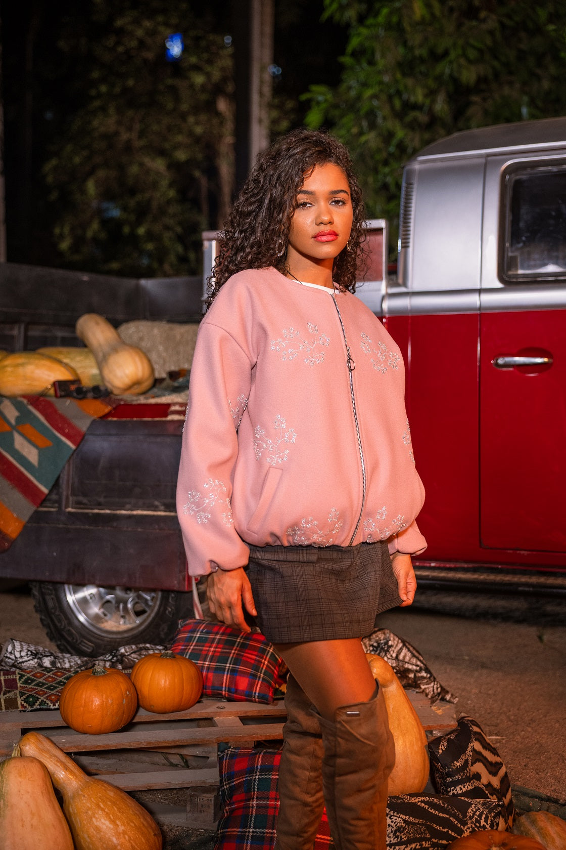 Woman in a pink sweatshirt standing next to a vintage red truck with pumpkins.
