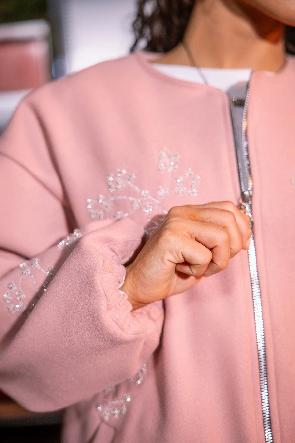 Close-up of a pink jacket with embellishments and a person's hand.