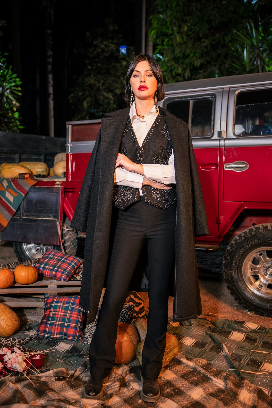 Woman in formal attire standing in front of a red truck with pumpkins and plaid blankets.
