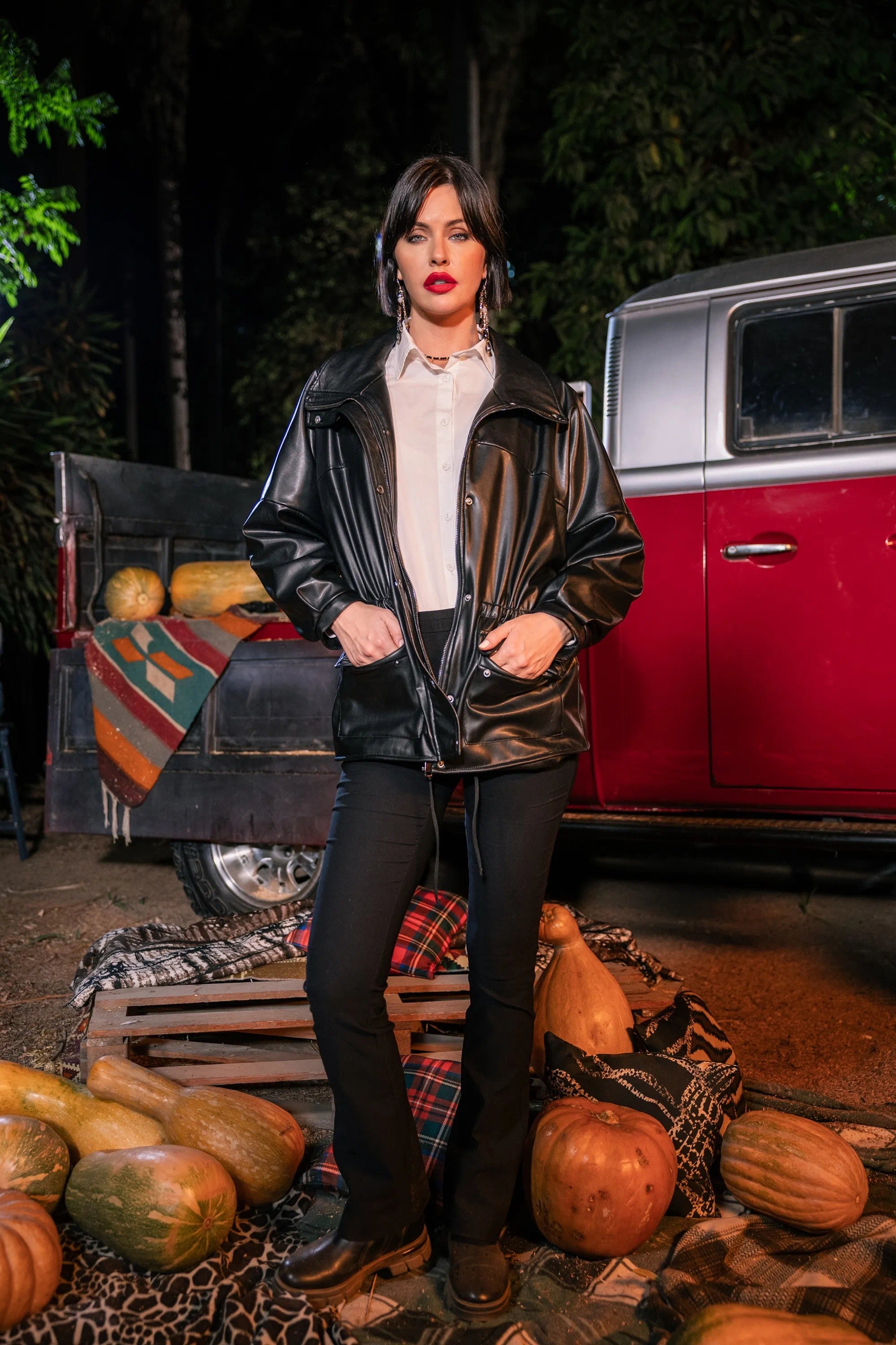 Woman in a leather jacket standing in front of a red truck with pumpkins around.