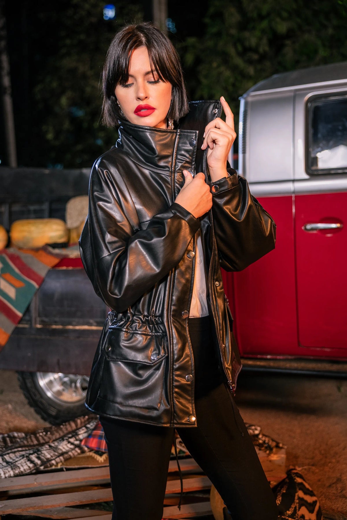 Woman in a shiny black jacket holding a phone with a vintage car in the background