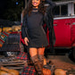 Woman in a black dress and knee-high boots standing in front of a red truck with pumpkins around.