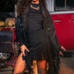 Woman in a black outfit with a fringe jacket standing in front of a vintage car.
