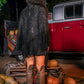 Person wearing a black fringe jacket and knee-high boots standing in front of a red truck with pumpkins around.