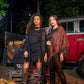Two women standing in front of a red truck with pumpkins at night.
