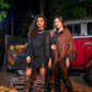 Two women standing in front of a red truck with pumpkins at night.